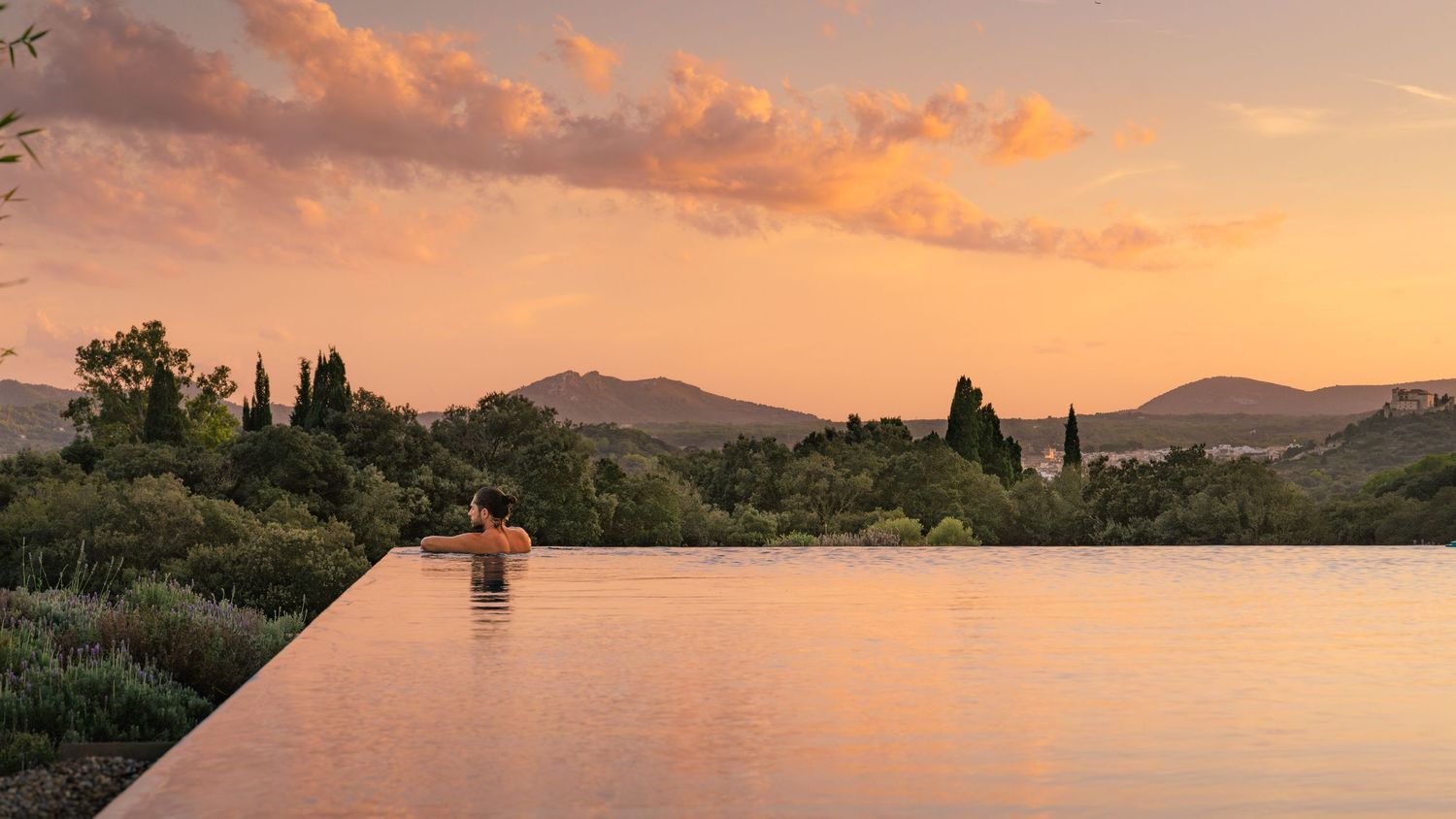 Serene pool view at sunset with mountains and cypress trees silhouetted against orange sky.