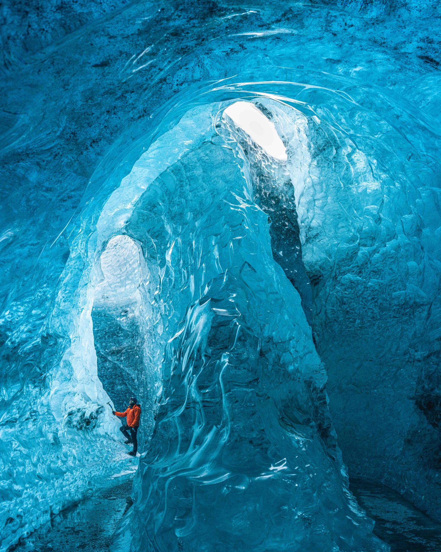 Explorer inside stunning blue ice cave with ethereal glacial formations.