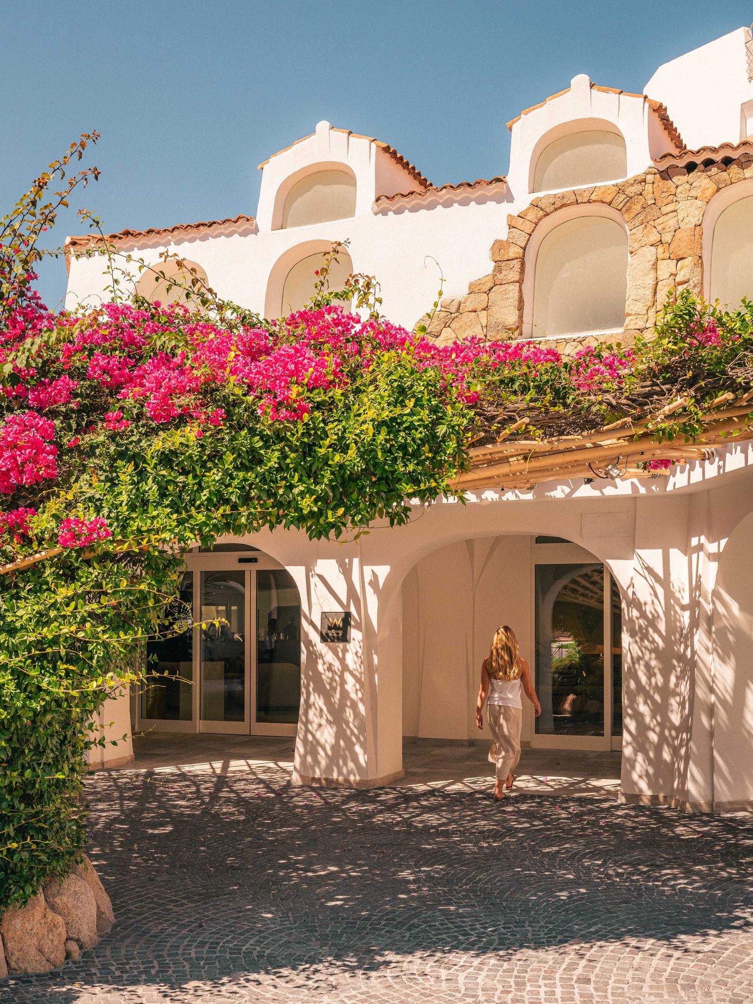 Mediterranean style villa exterior with pink bougainvillea flowers and white arched architecture.