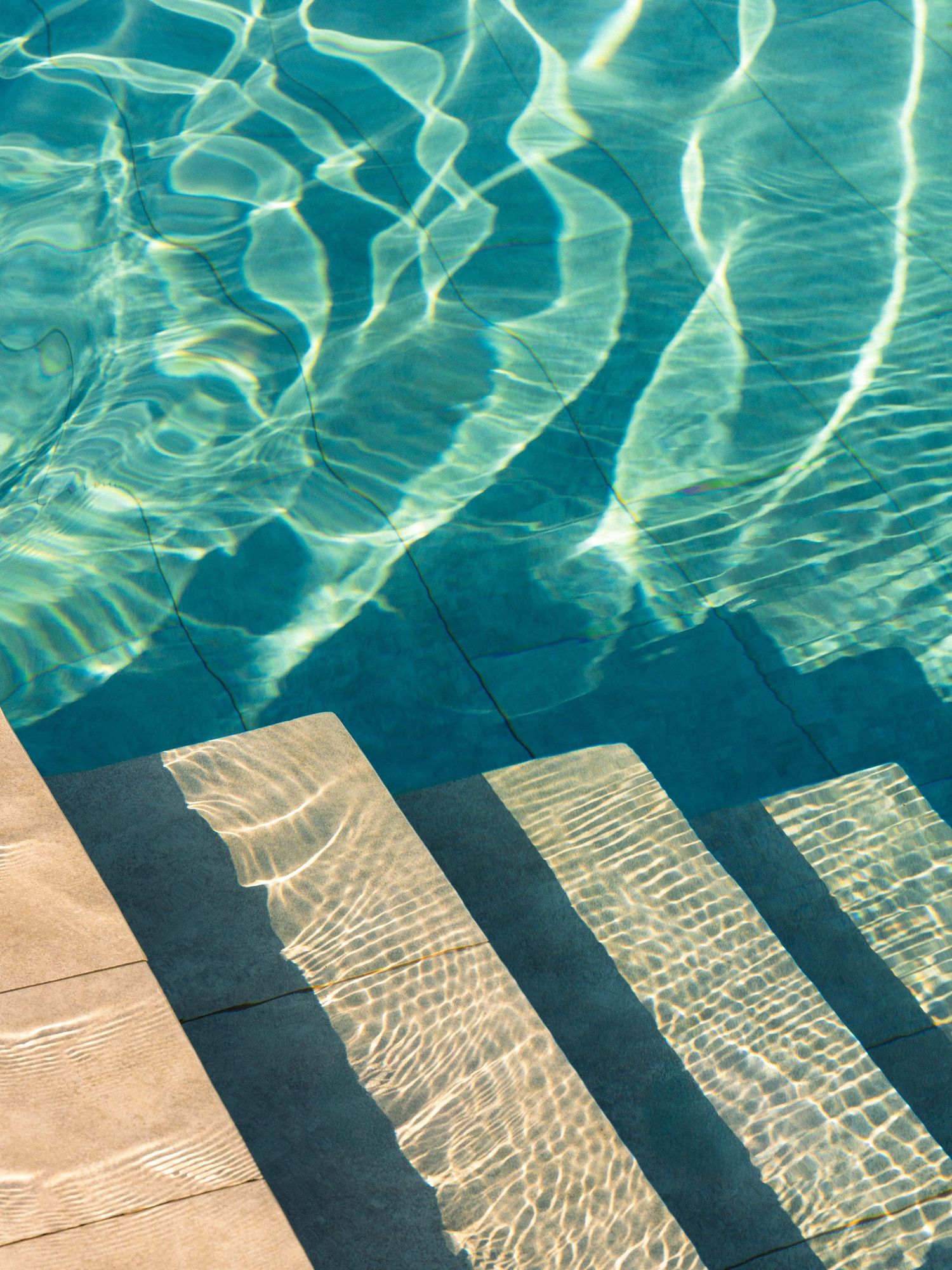 Sunlight creates mesmerizing ripple patterns on turquoise pool steps underwater.