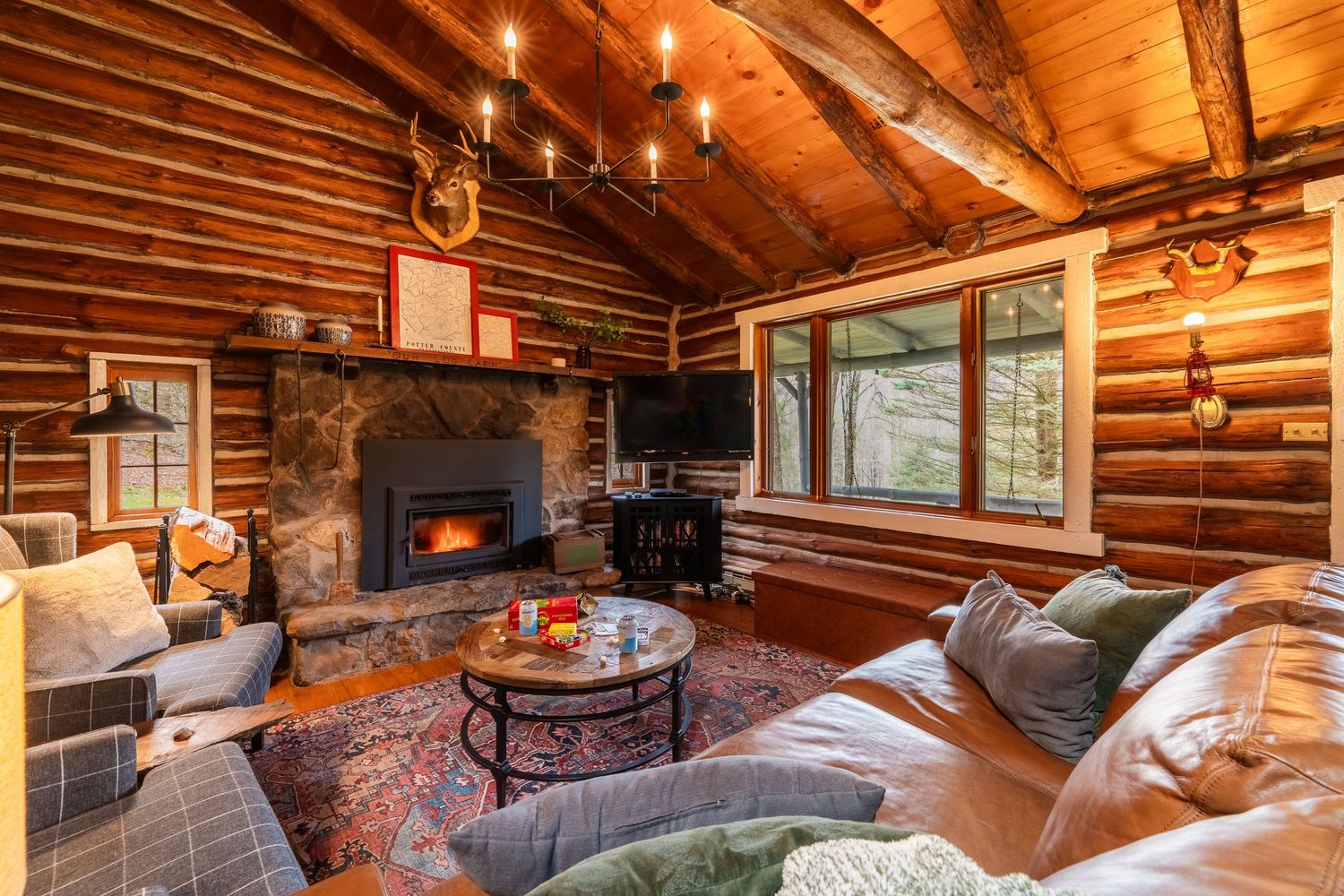 Cozy log cabin living room with rustic wood walls, exposed beams, stone fireplace, and candlelit decorative accents.