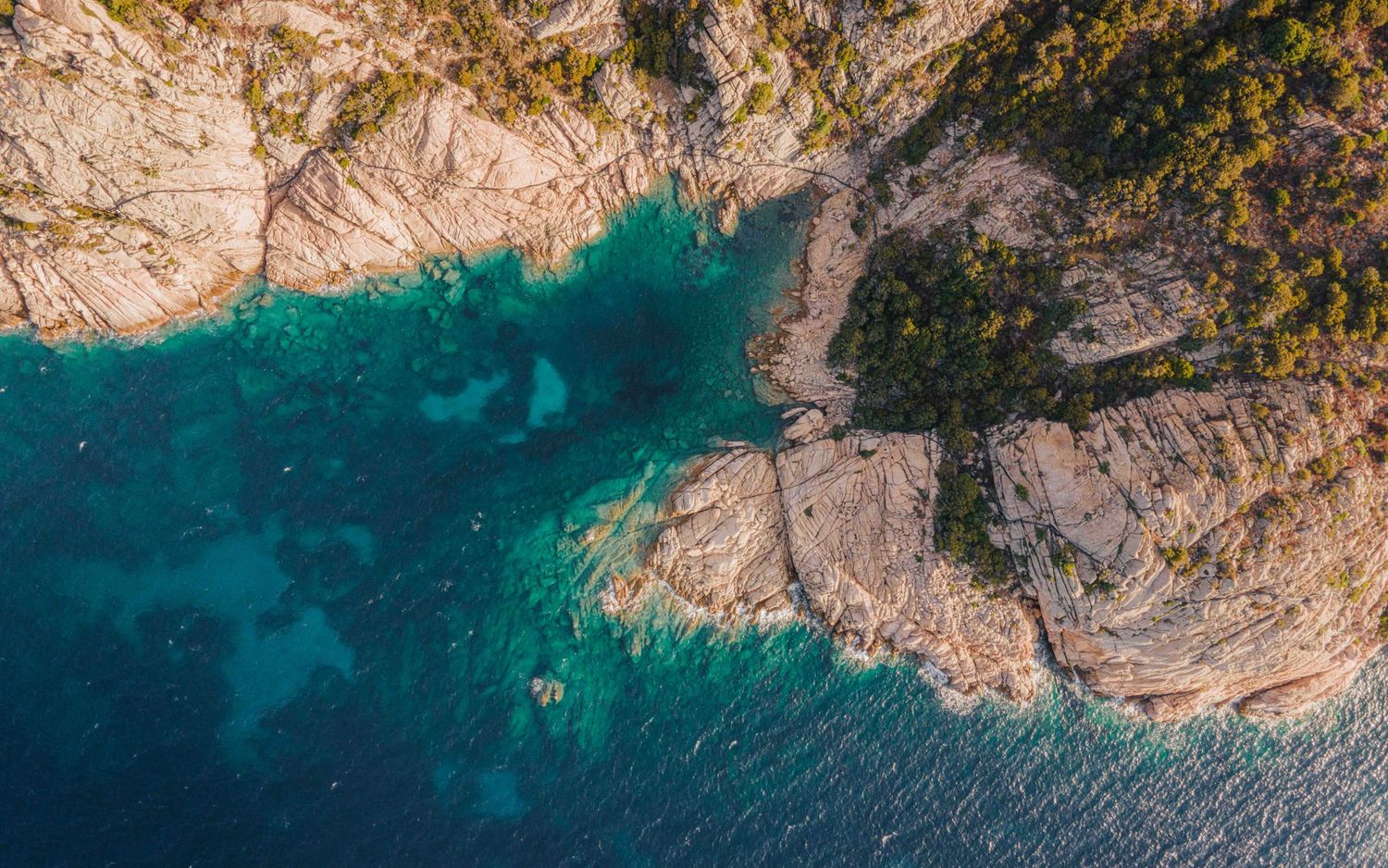 Aerial view of rocky coastline meeting turquoise Mediterranean waters.
