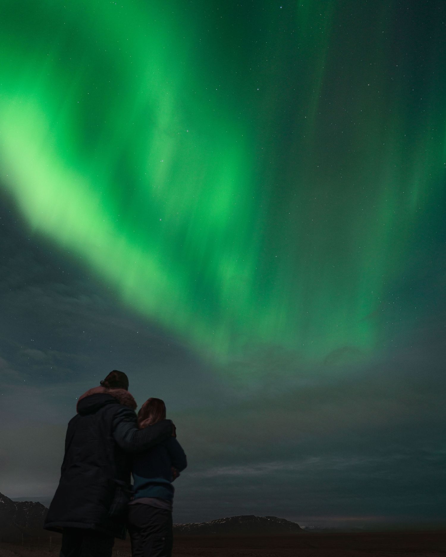Silhouettes watching the Northern Lights dance across the night sky in vibrant green hues.