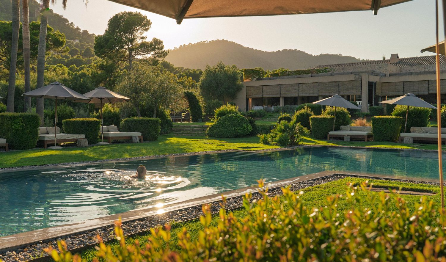 Luxury resort pool area with mountain views and umbrella seating at sunset.