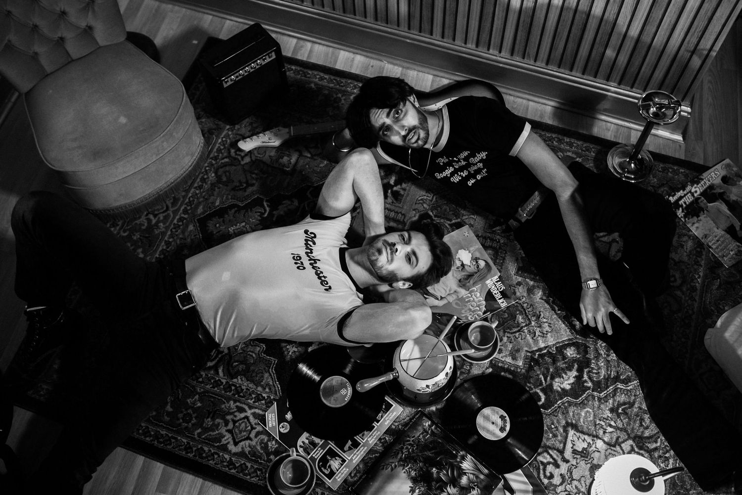 Black and white photo of people relaxing on floor with drinks and snacks.