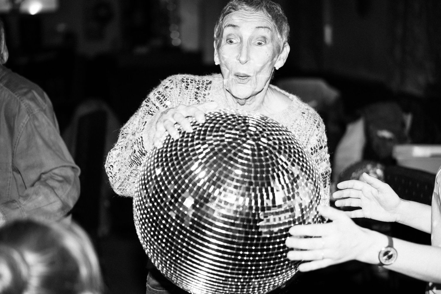 Black and white photo showing someone holding a large disco ball in a dimly lit venue.