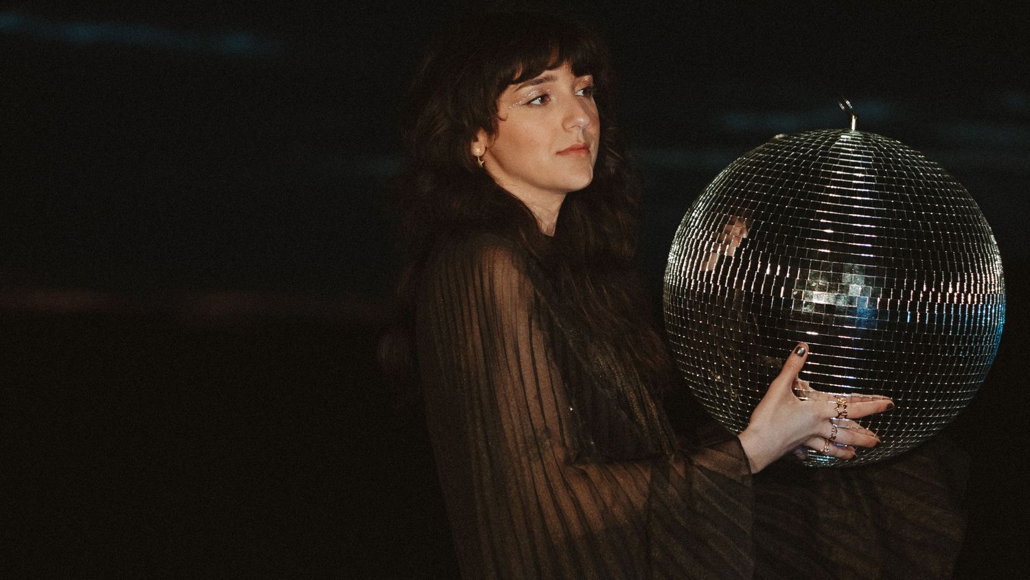 Moody sequence showing a person posing with a disco ball in dark lighting.