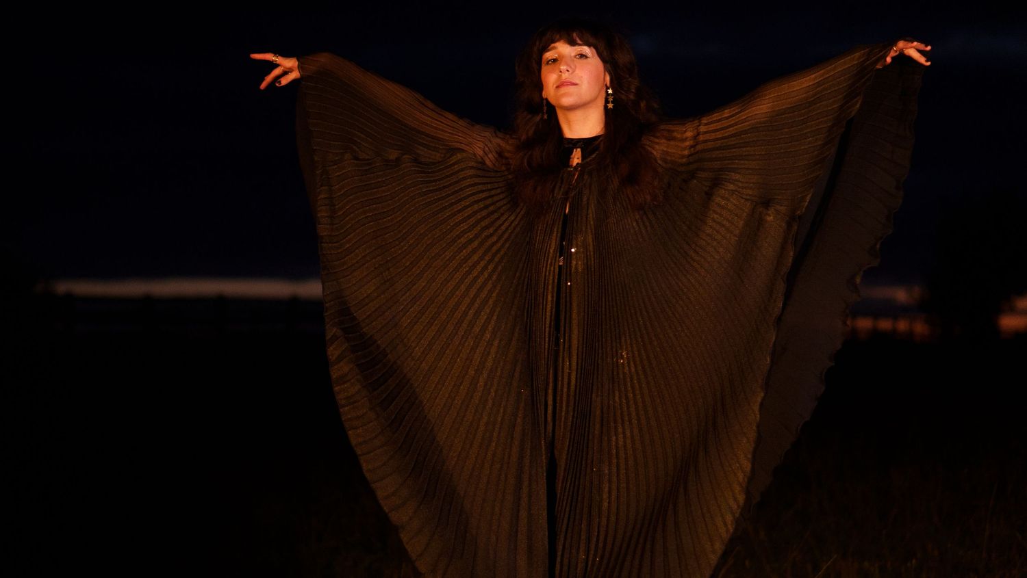 Dark atmospheric photo of a figure in dramatic lighting with wings or fabric spread out.