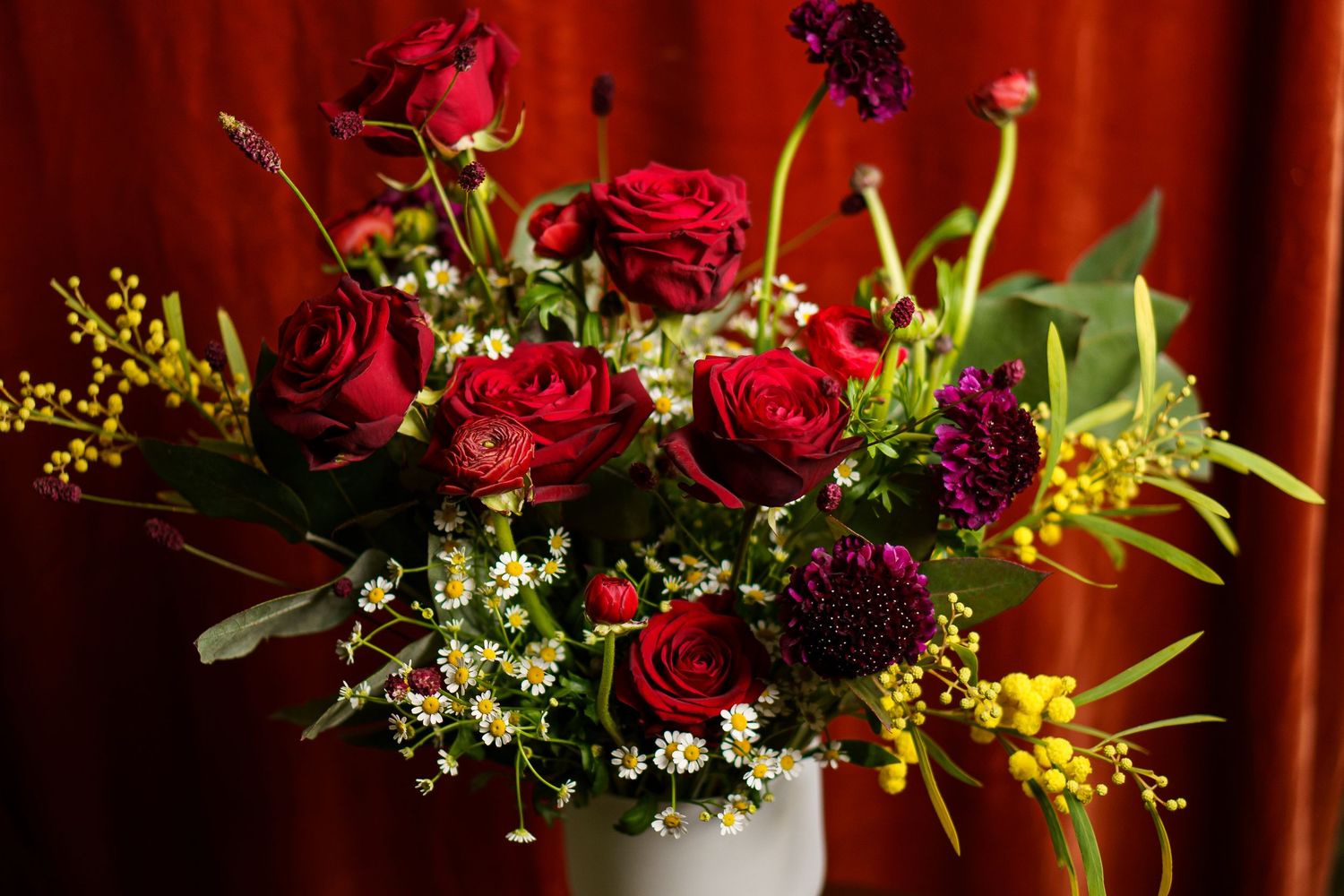 A collection of vibrant floral arrangements featuring deep red roses and yellow accent flowers against a dark background.
