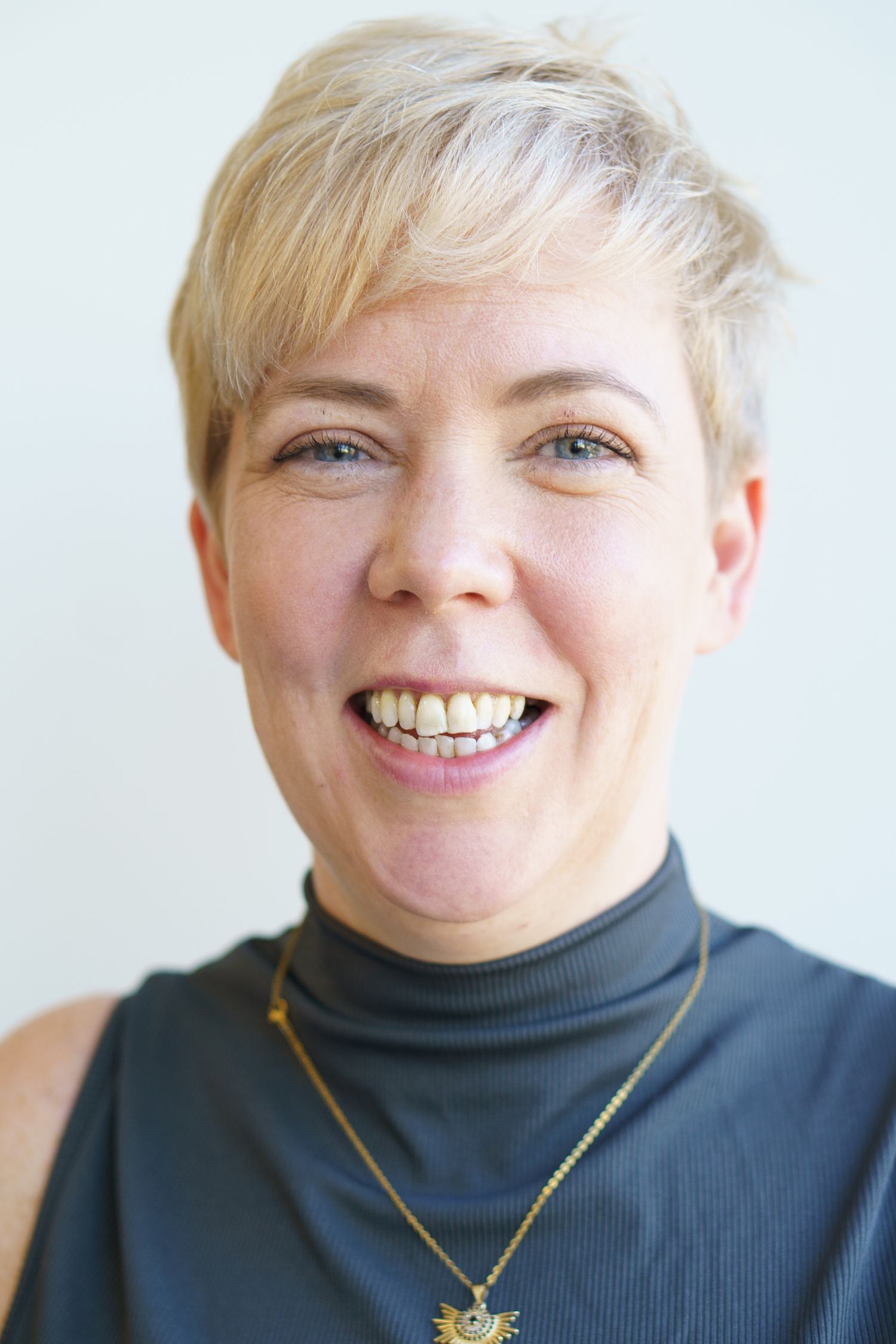 A series of four headshots showing different expressions while wearing a dark turtleneck and gold necklace.