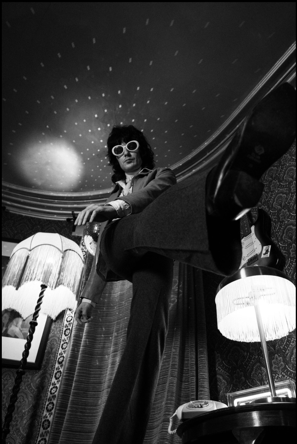 A vintage-style black and white photo of someone in sunglasses posing beneath decorative ceiling lights.