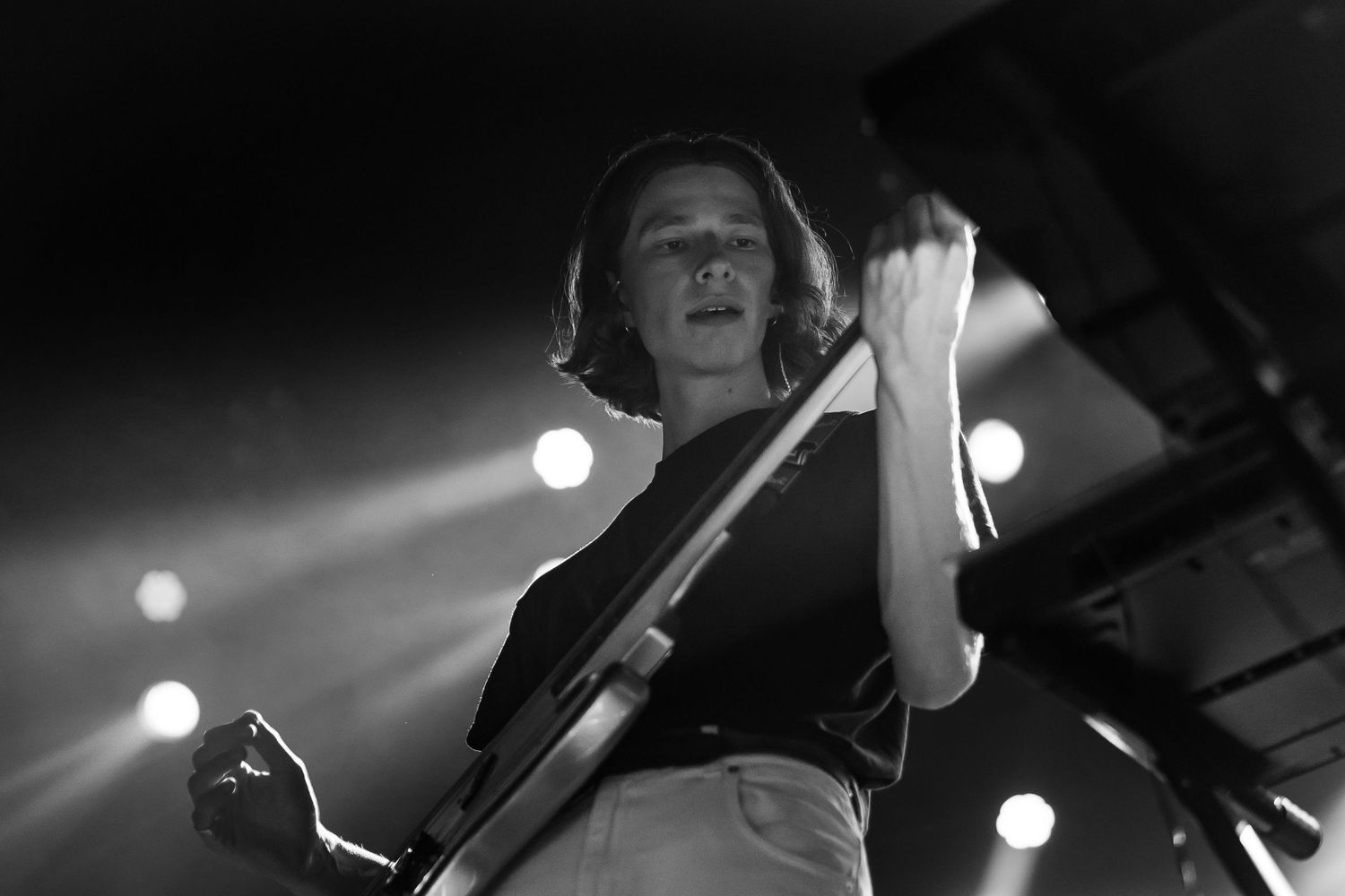 Black and white photo of a guitarist performing on stage with dramatic backlighting during a live concert.