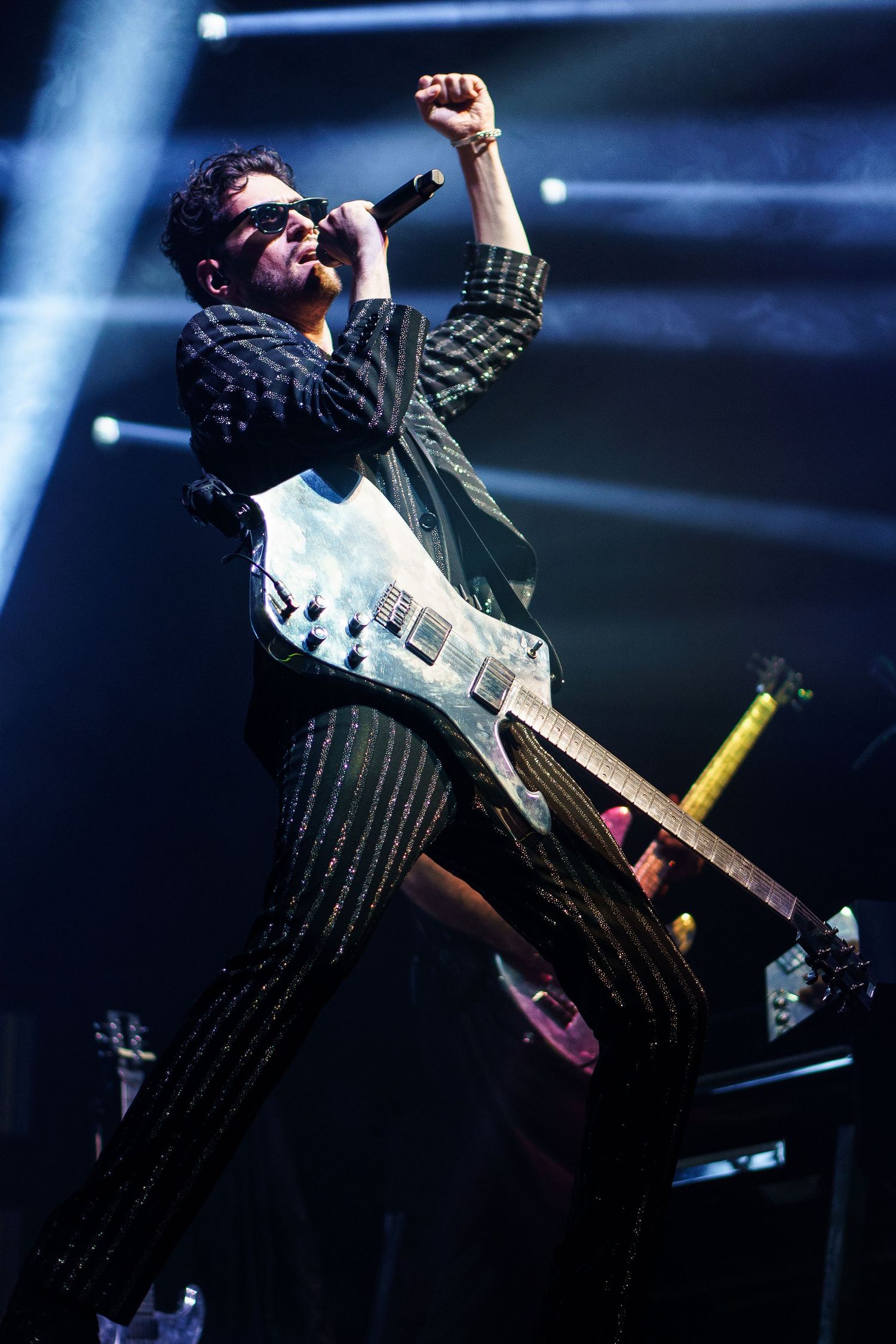 Rock musician performing on stage with guitar, wearing pinstripe suit and sunglasses under dramatic blue stage lights.