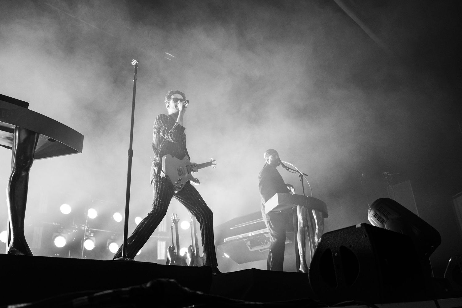 Black and white concert photo of two musicians performing on a smoky stage with dramatic backlighting.