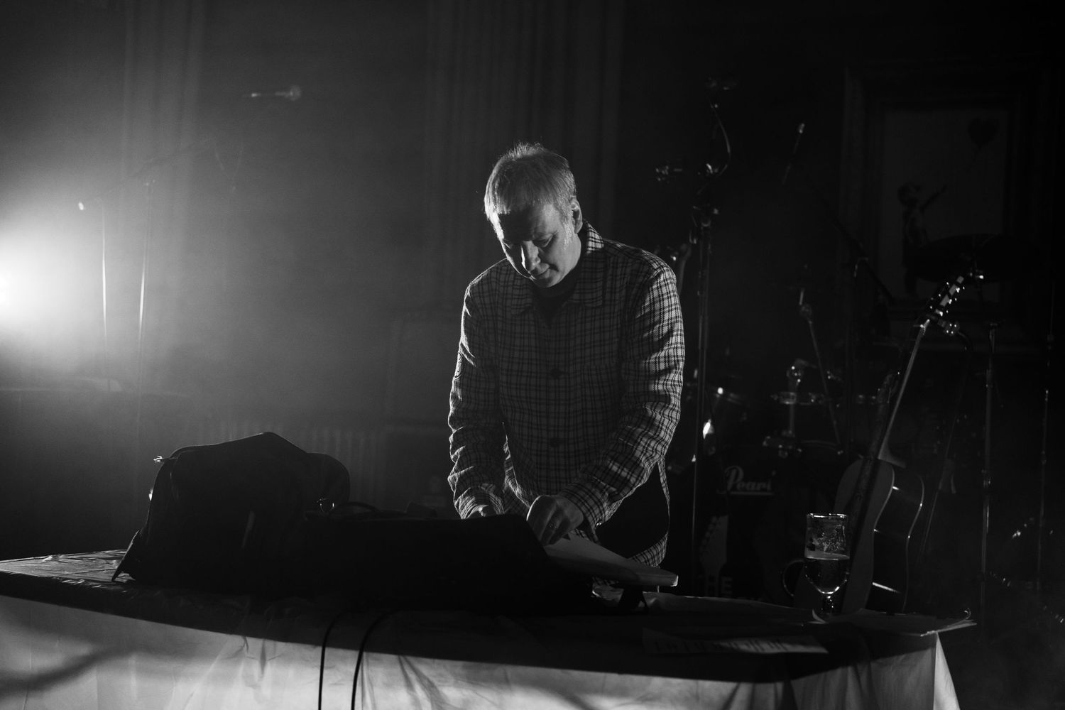 Black and white photo of a DJ performing at a dimly lit venue with equipment on a table.