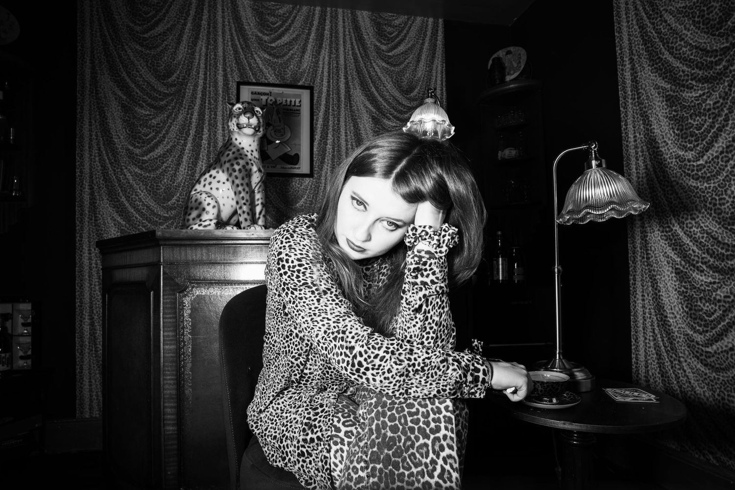 Black and white photo of someone in leopard print clothing against draped curtains.