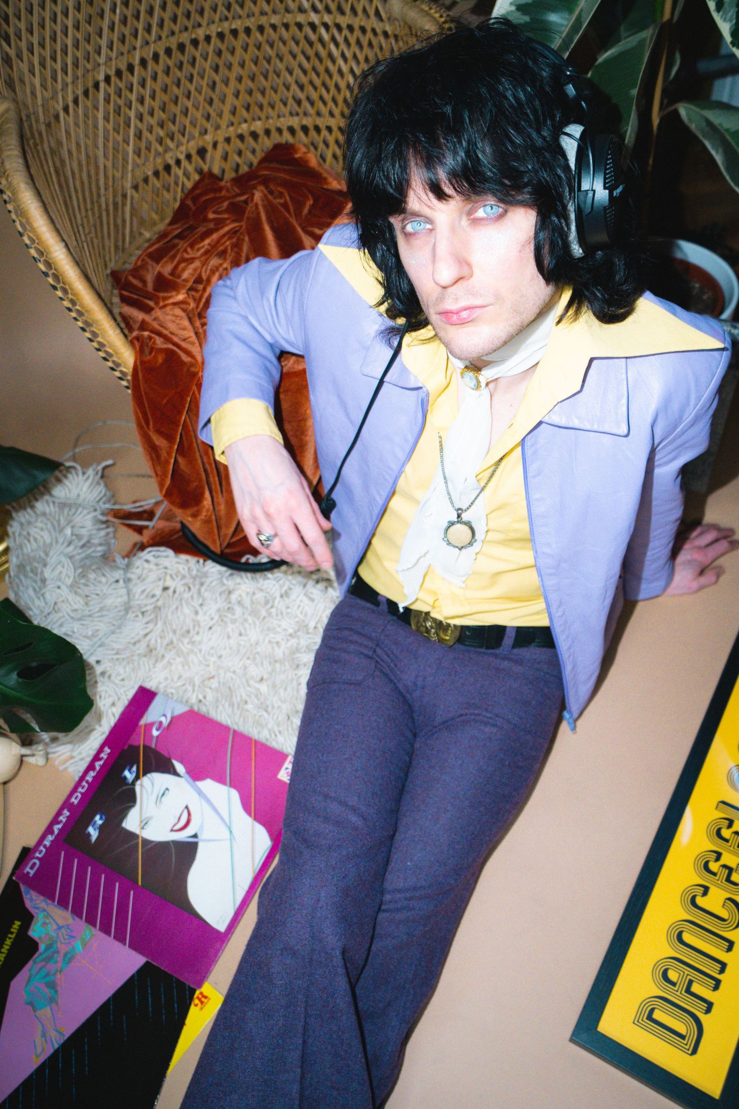 A 1970s style photo showing someone in a purple suit and yellow shirt lounging with headphones.