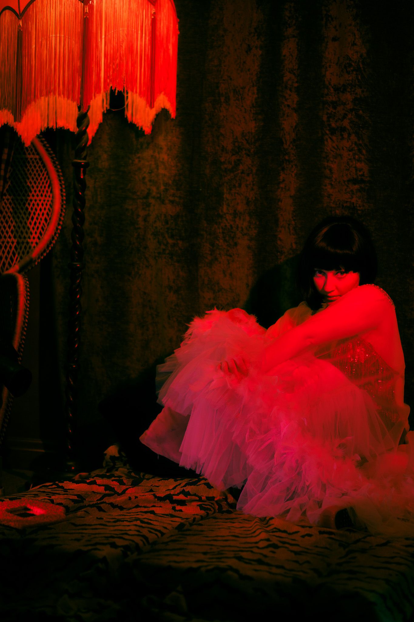 Dramatic red-lit silhouette of a figure in a tulle dress against a dark background.