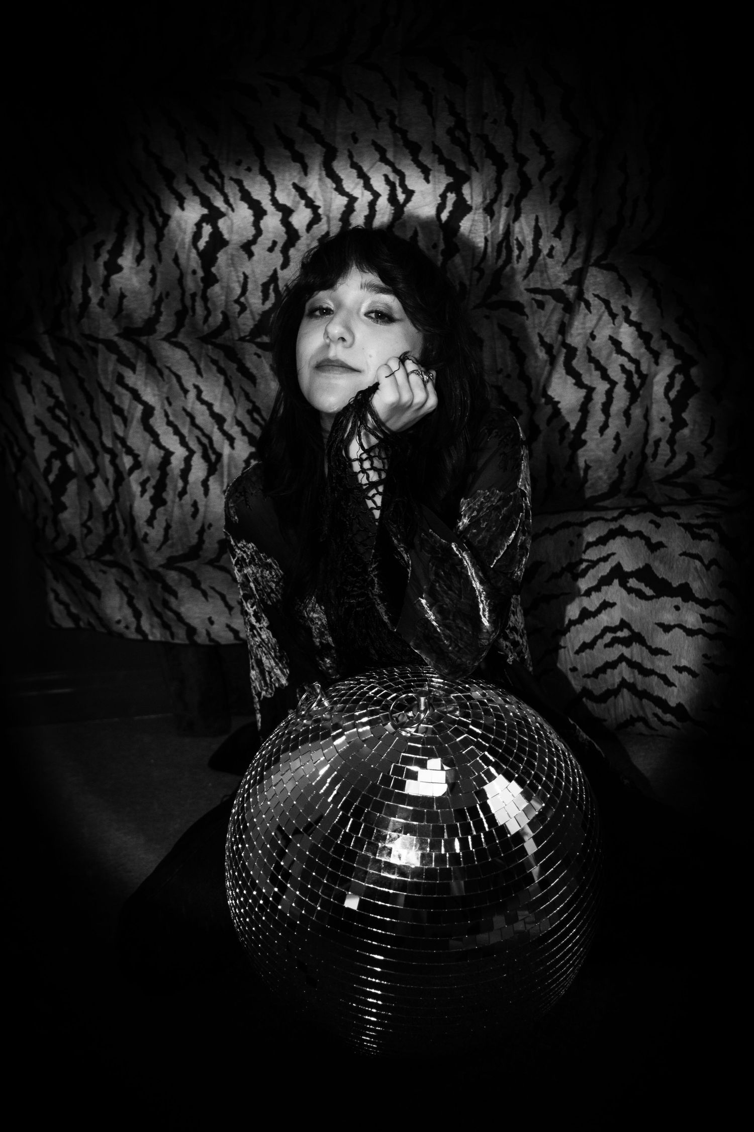 Woman in black outfit poses with disco ball in moody black and white photo with tiger print backdrop.