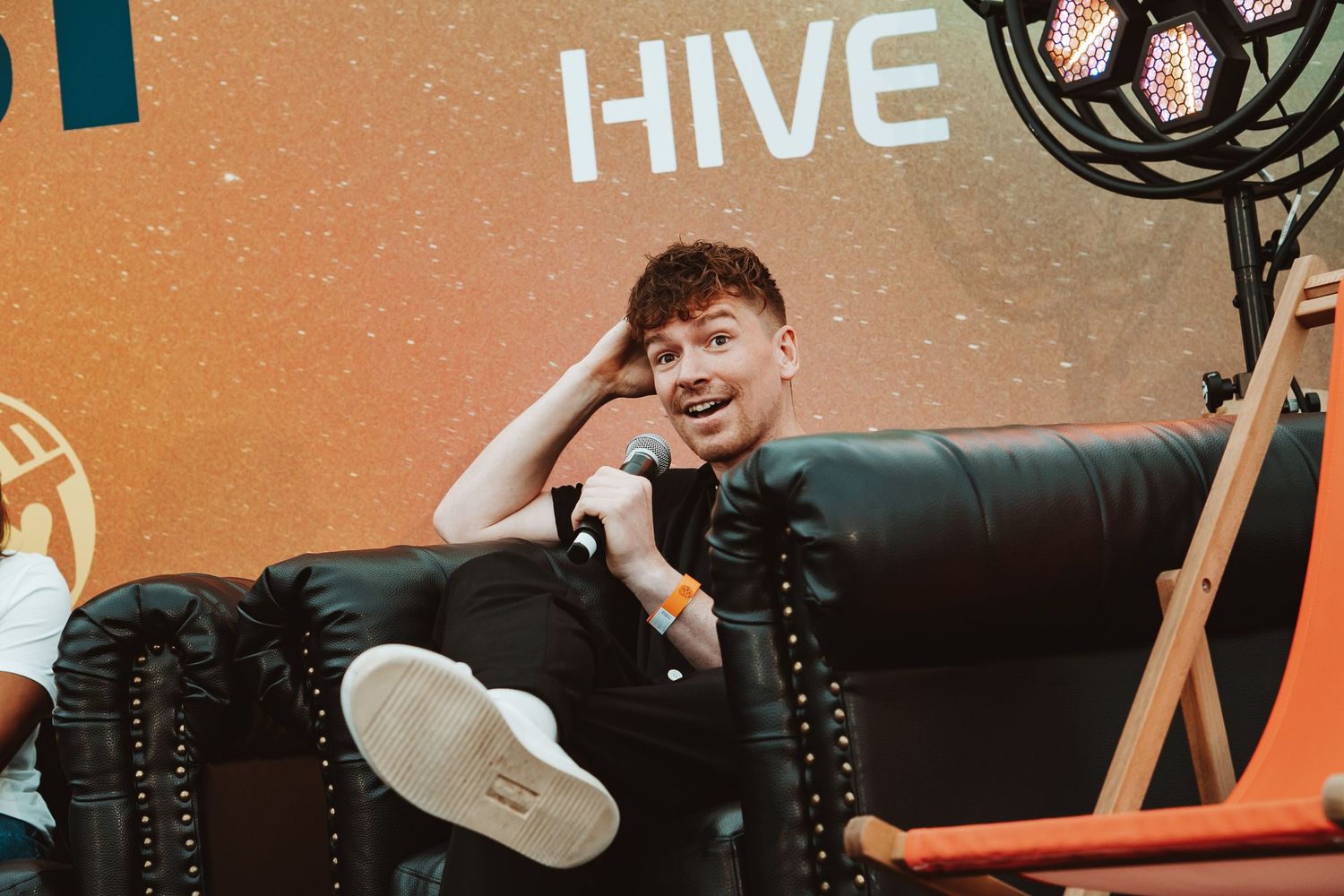 Someone lounges casually on a black leather couch against an orange wall with the word 'HIVE' displayed.