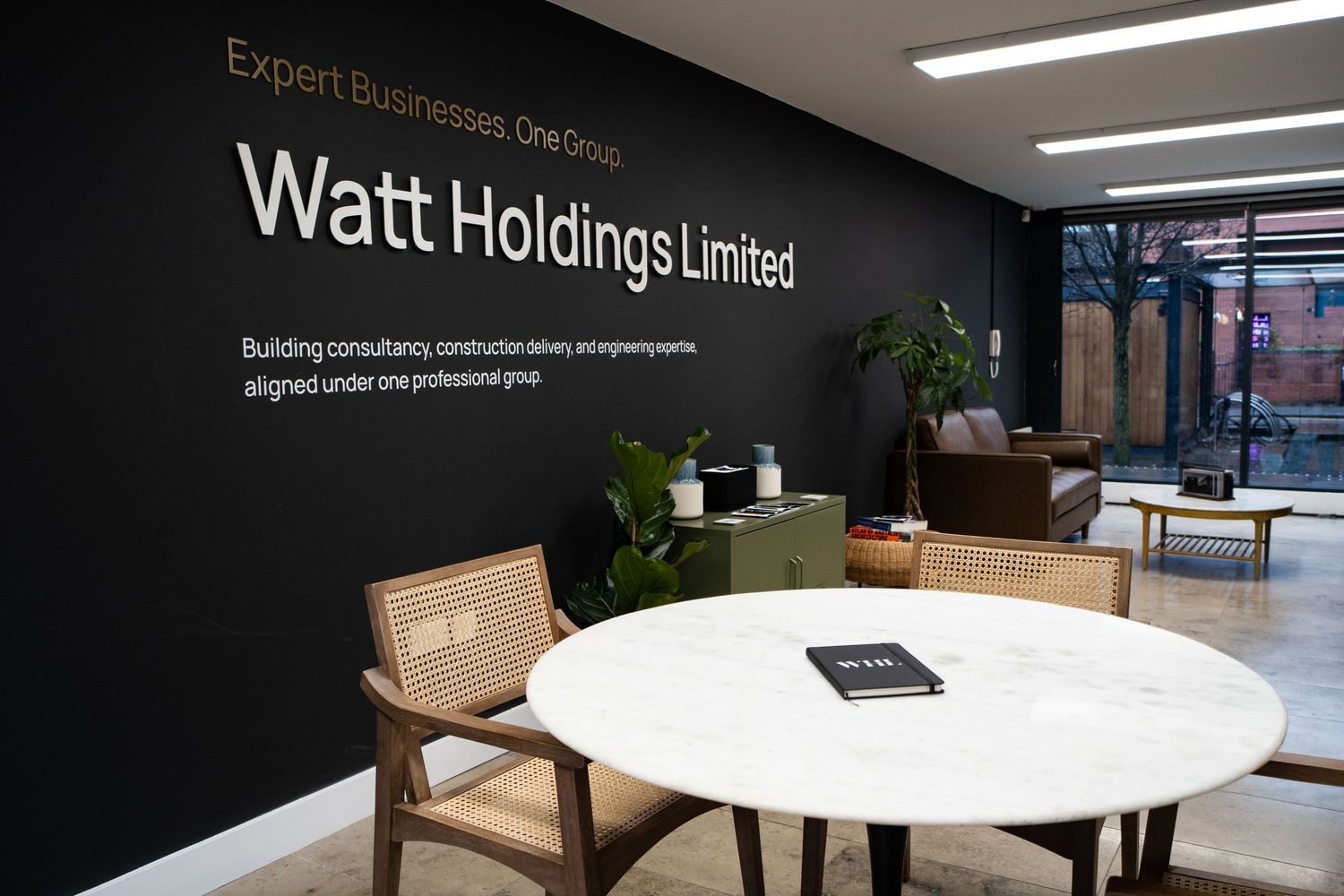 Modern office interior with sleek white tables and dark walls showcasing Watt Holdings Limited branding.
