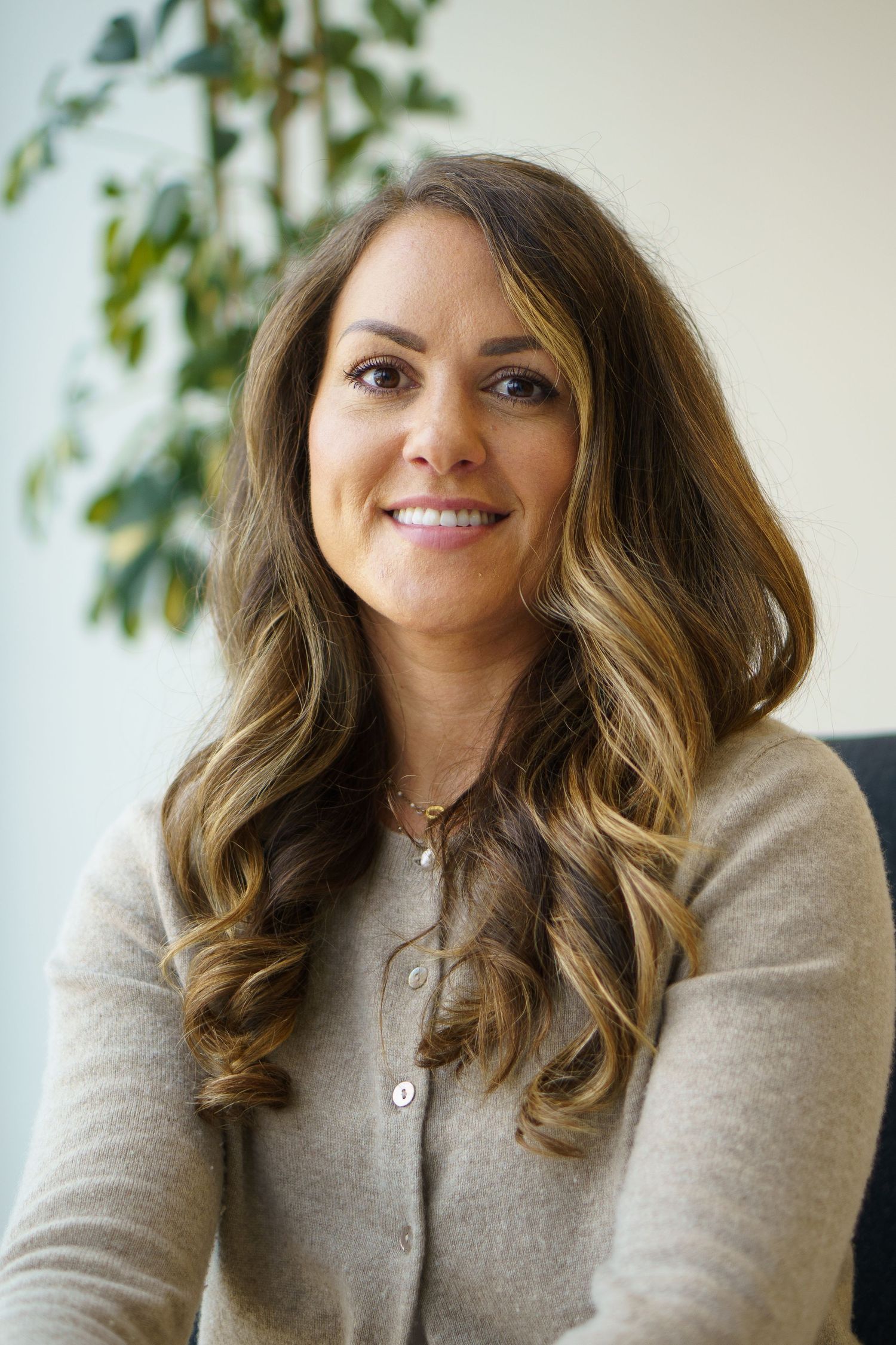 Professional headshots showing warm smiles and wavy brown hair against a light background with greenery.