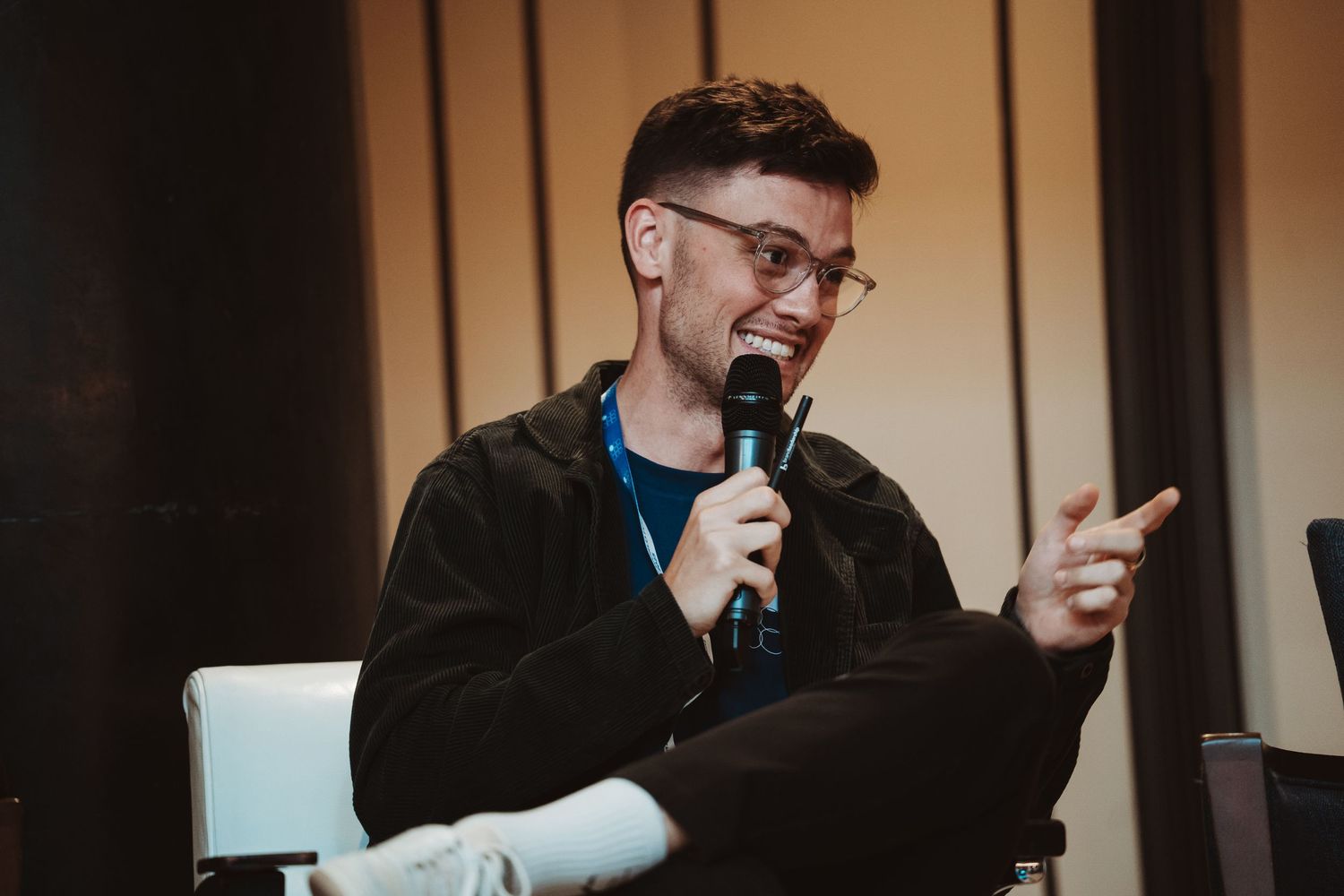 A person in glasses speaks into a microphone while seated at a table during what appears to be a panel discussion.