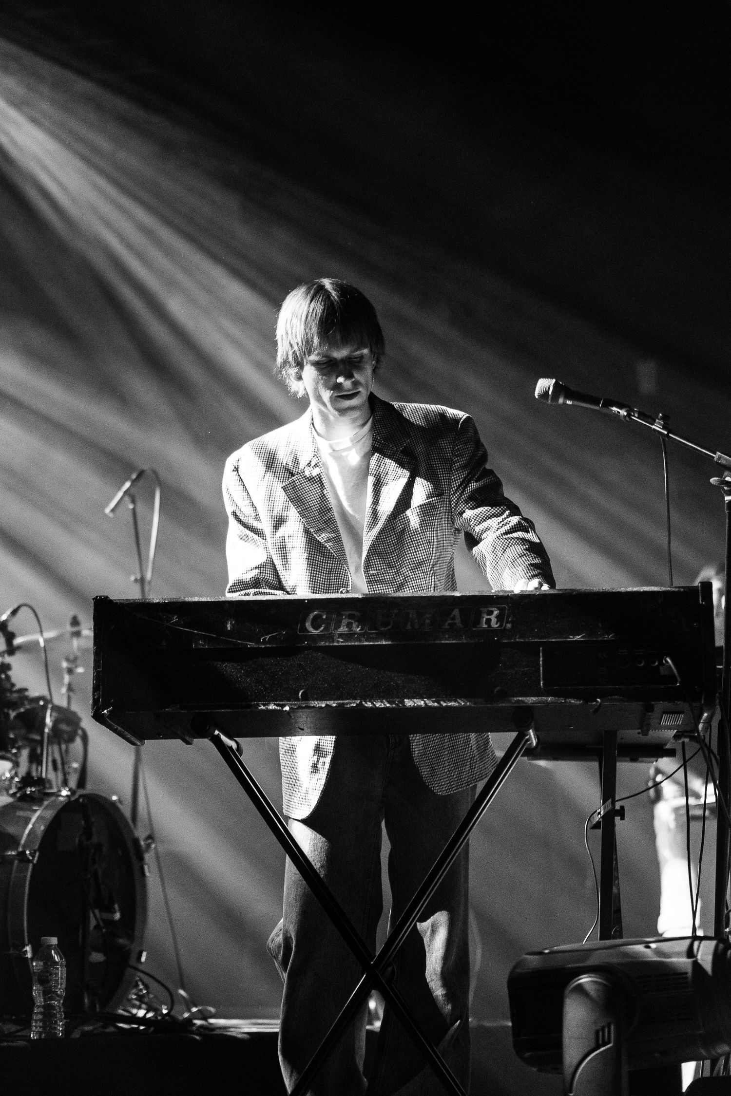 Musician playing a Kawai keyboard on stage in black and white with dramatic spotlight rays.