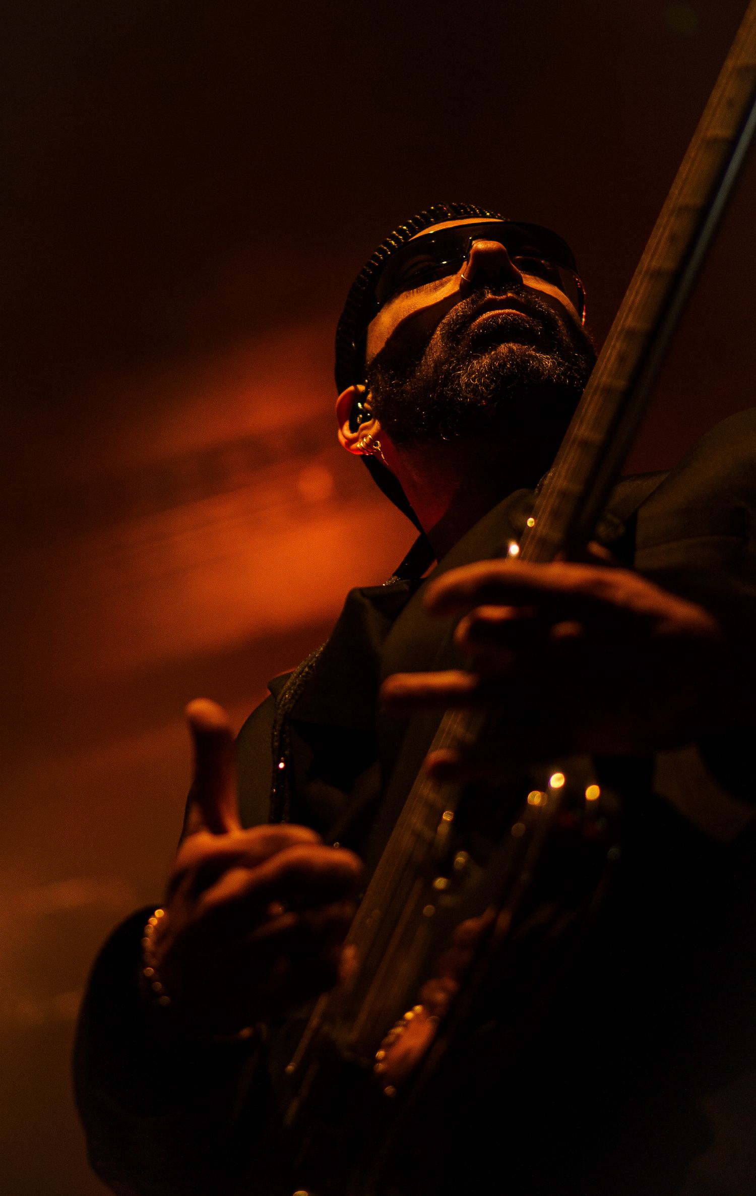Atmospheric orange-tinted portrait of musician with guitar shot from below against dark background.