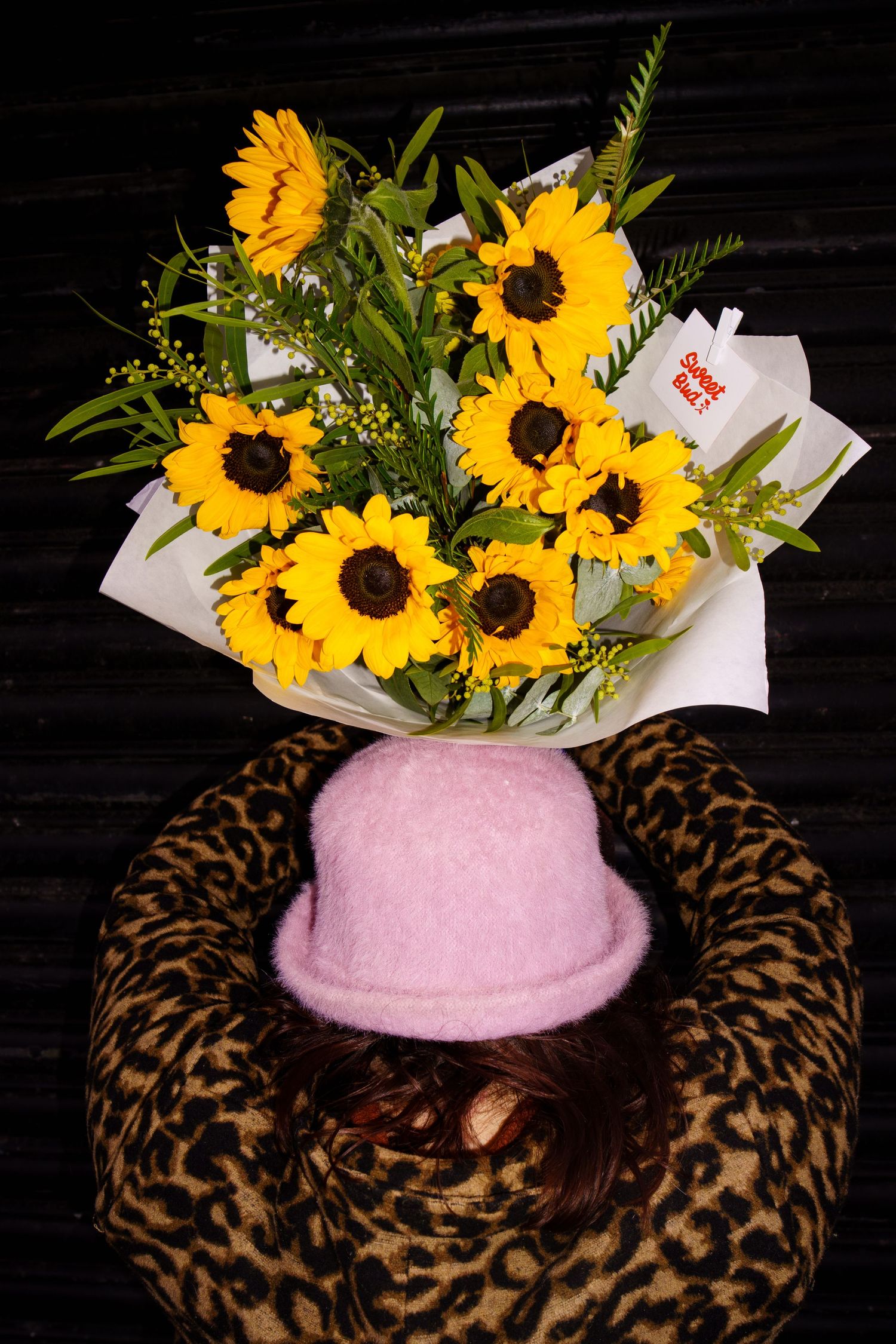 Bright yellow sunflowers arranged in a bouquet displayed in a pink vase with leopard print decor on a dark background.