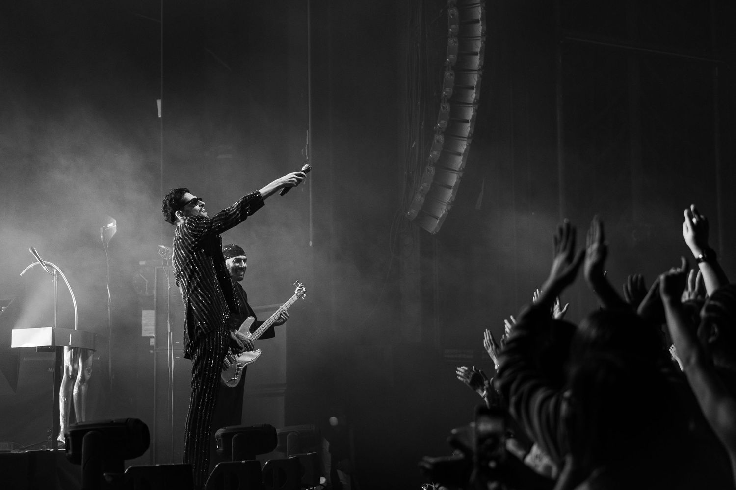 Black and white concert photo showing performer on stage with crowd raising hands in silhouette.