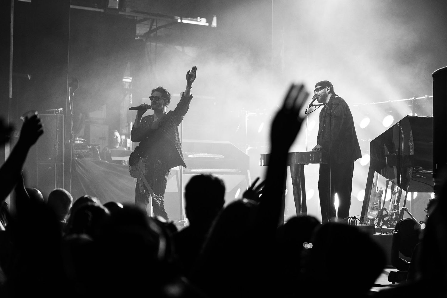Black and white concert photo of two performers on stage with dramatic lighting and an energetic crowd.