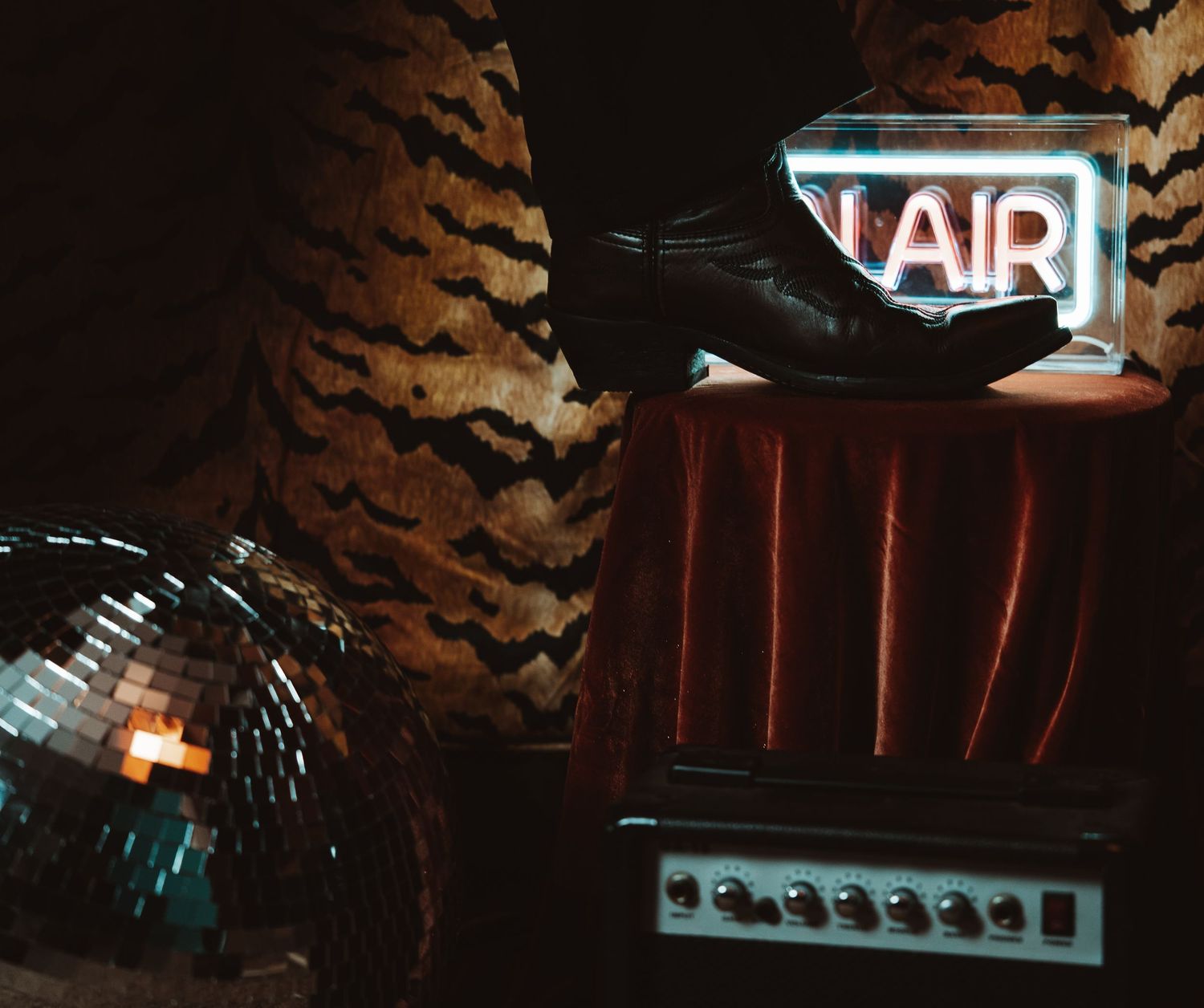 Retro AIR neon sign glowing beside a disco ball, black shoe, and guitar amp on tiger-print background.