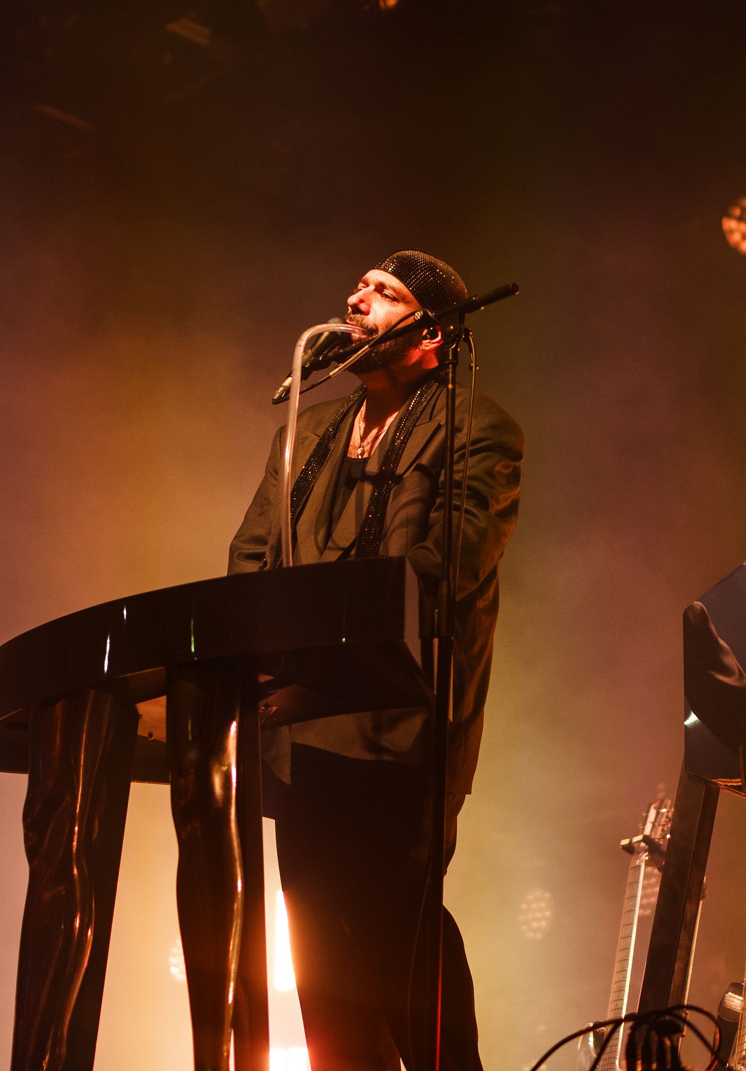 A musician performs on stage at a keyboard under dramatic orange stage lighting with fog effects at a live concert.