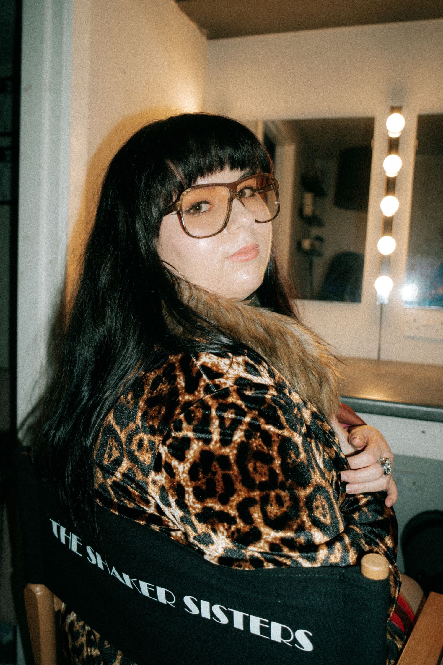 Person wearing glasses and leopard print clothing in a dressing room setting.