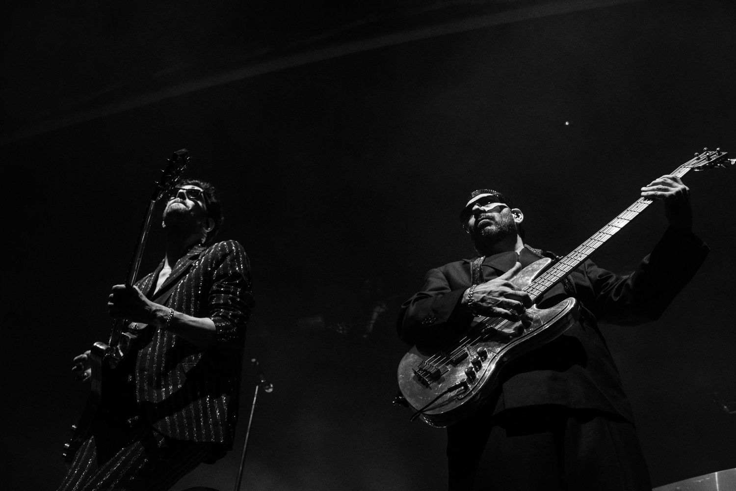 Two guitarists performing on stage in dramatic black and white lighting during a live concert.
