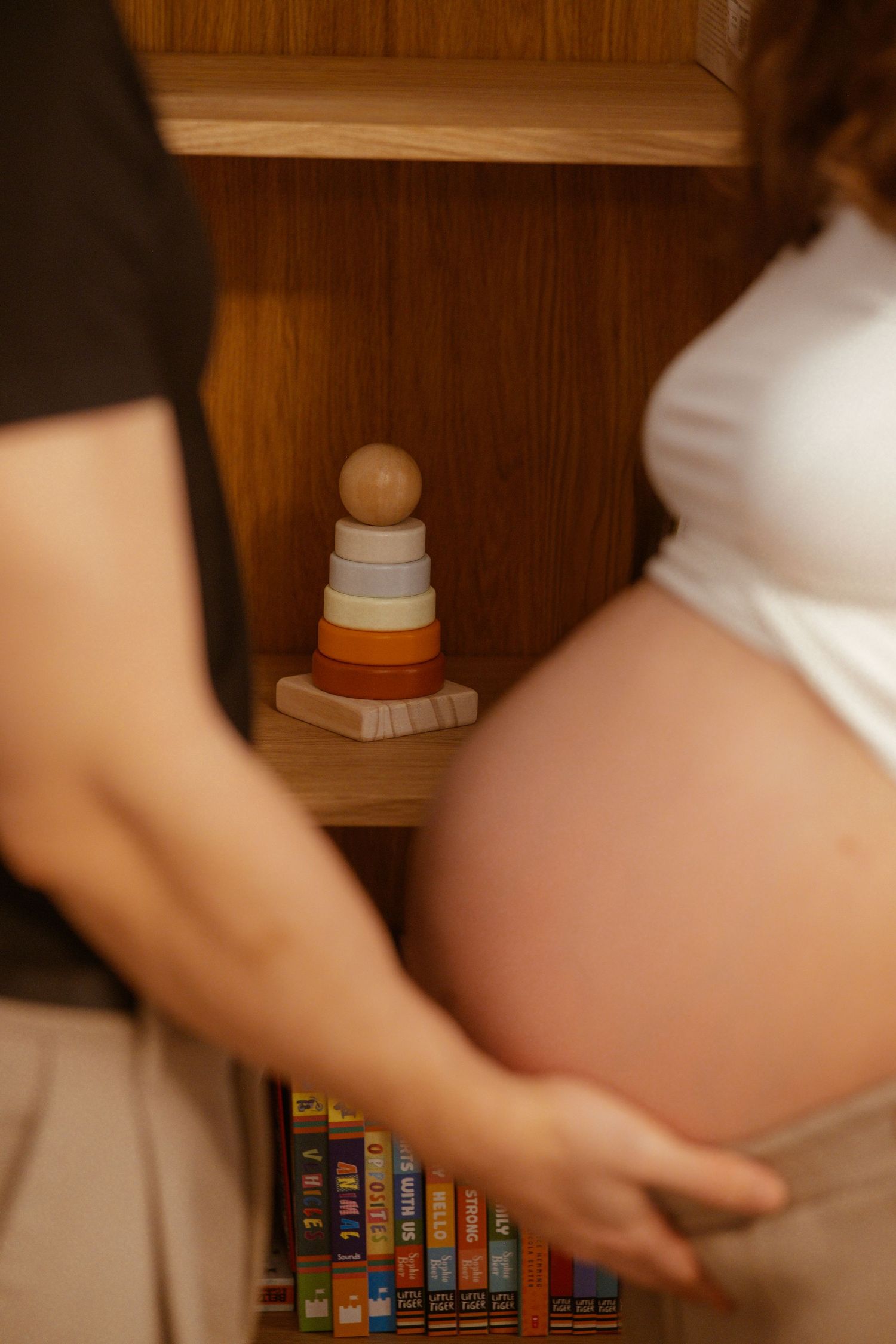 Close-up of a pregnant belly with father’s hands and a baby toy in the background, symbolic image of the baby’s arrival