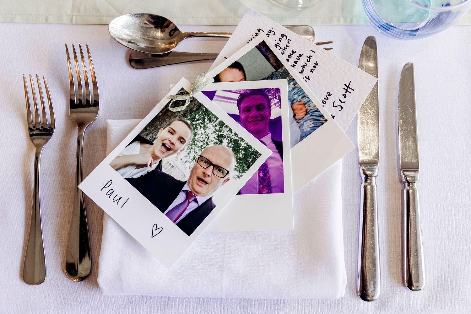 Polaroid wedding photos displayed as place card on white linen table setting with silverware.