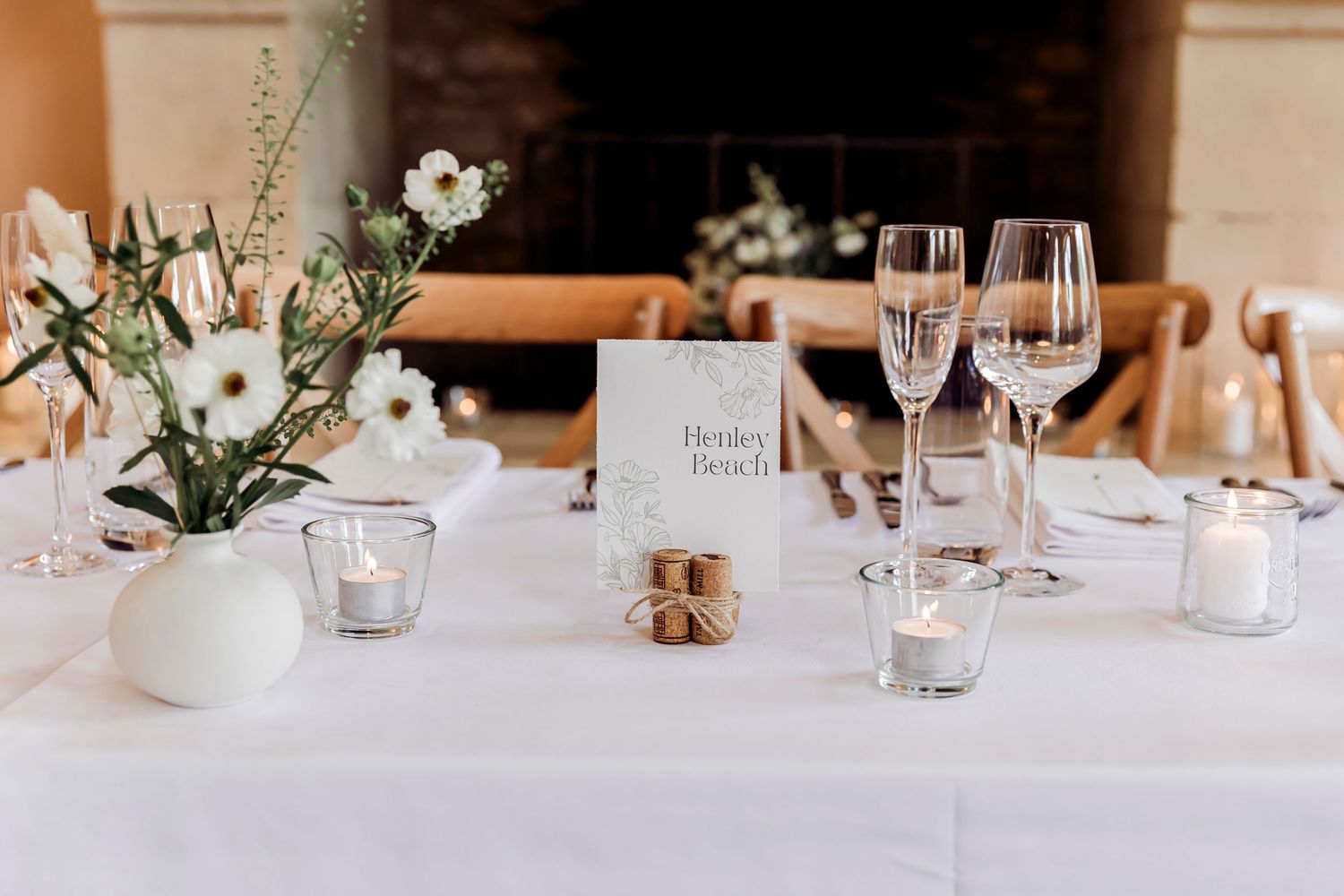 Elegant wedding reception table with white florals, champagne glasses, candles, and a place card.