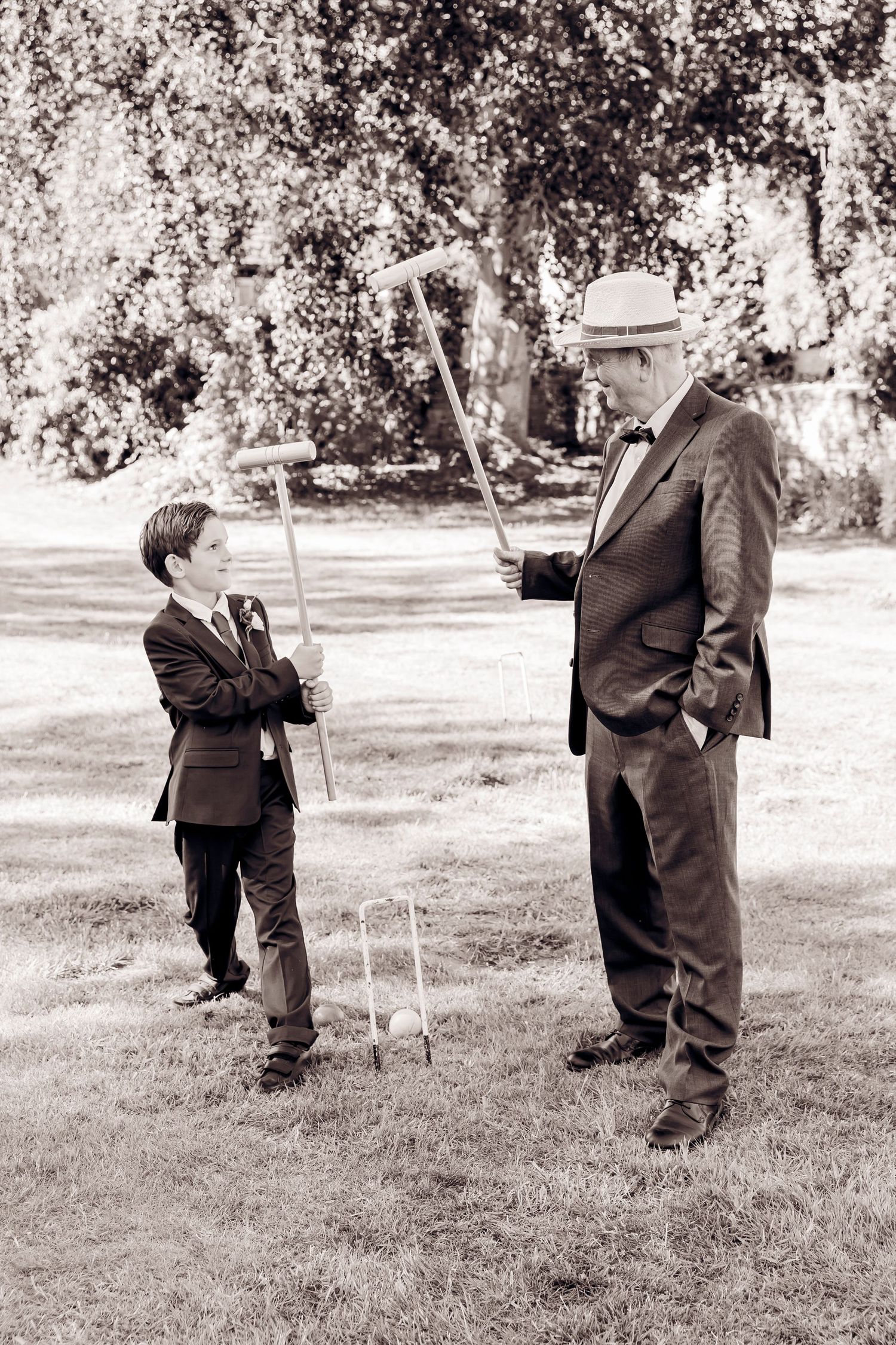 Black and white photo of a boy and elderly man playing croquet together at a wedding reception.