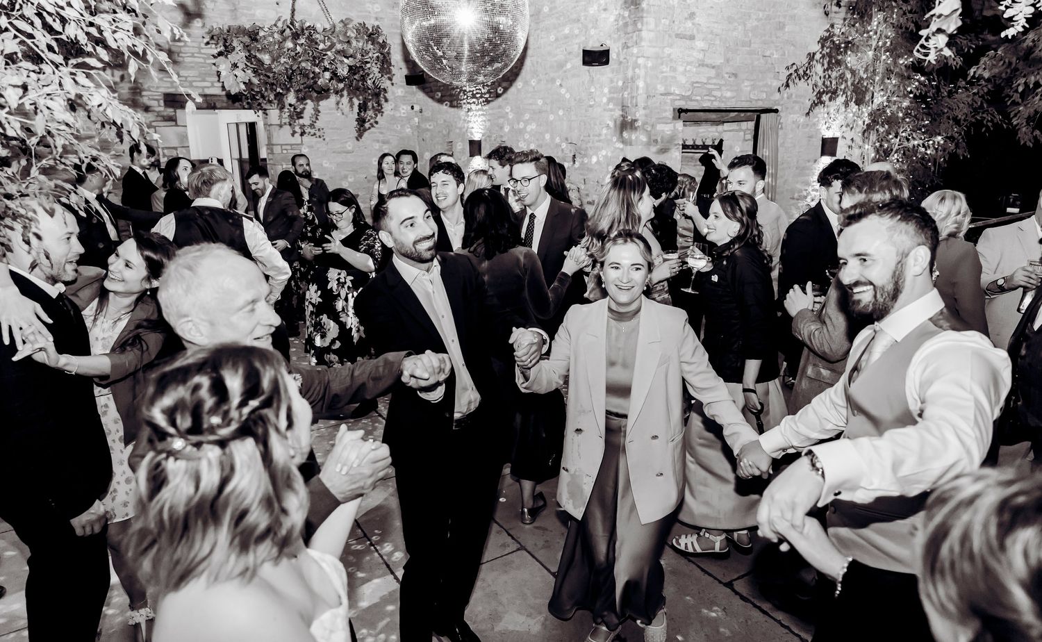 Wedding guests dancing joyfully together in black and white photo at lively reception.