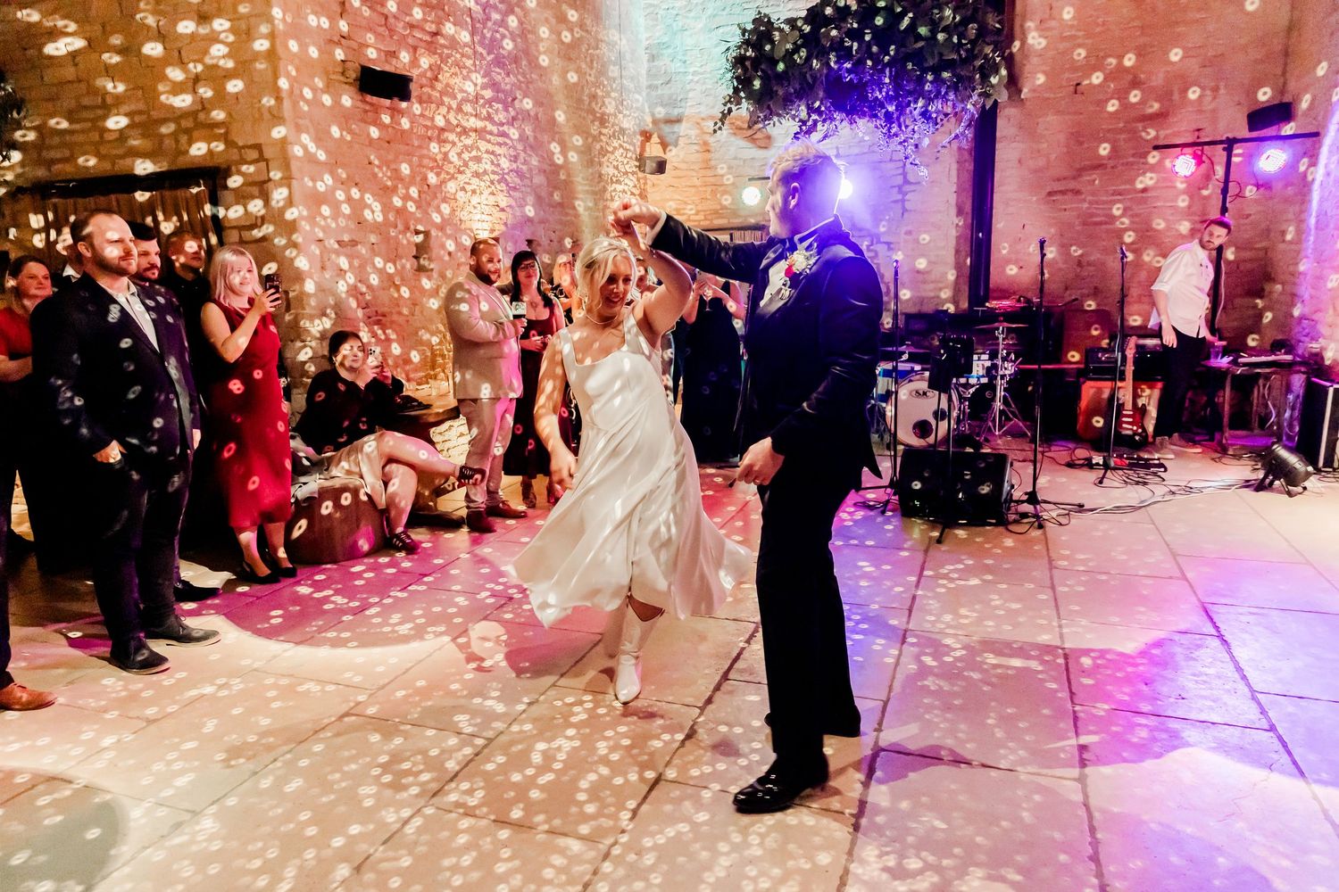 Couple shares romantic first dance with confetti falling at warmly lit wedding venue reception.