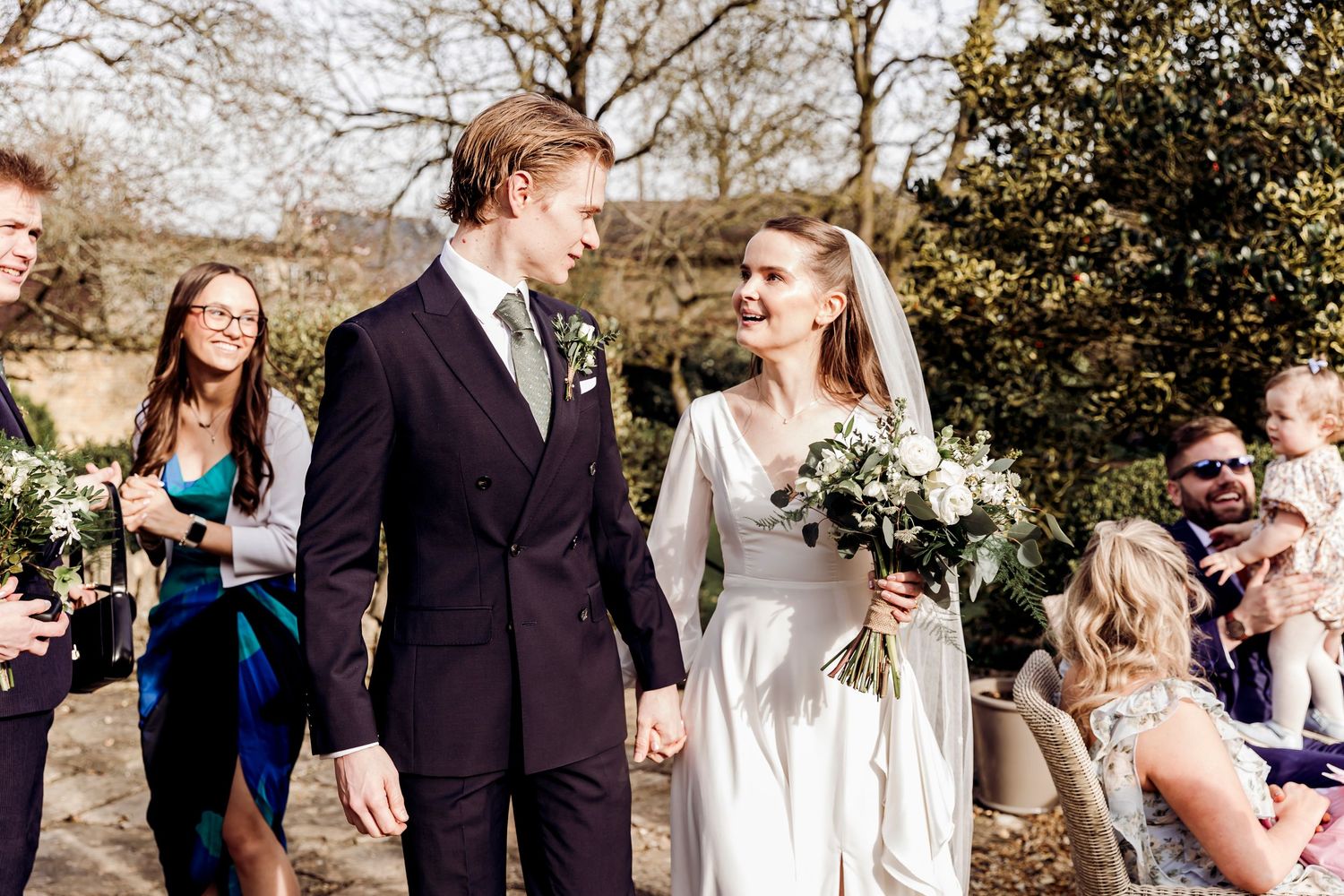 Newlyweds walking hand in hand through confetti shower with smiling wedding guests.