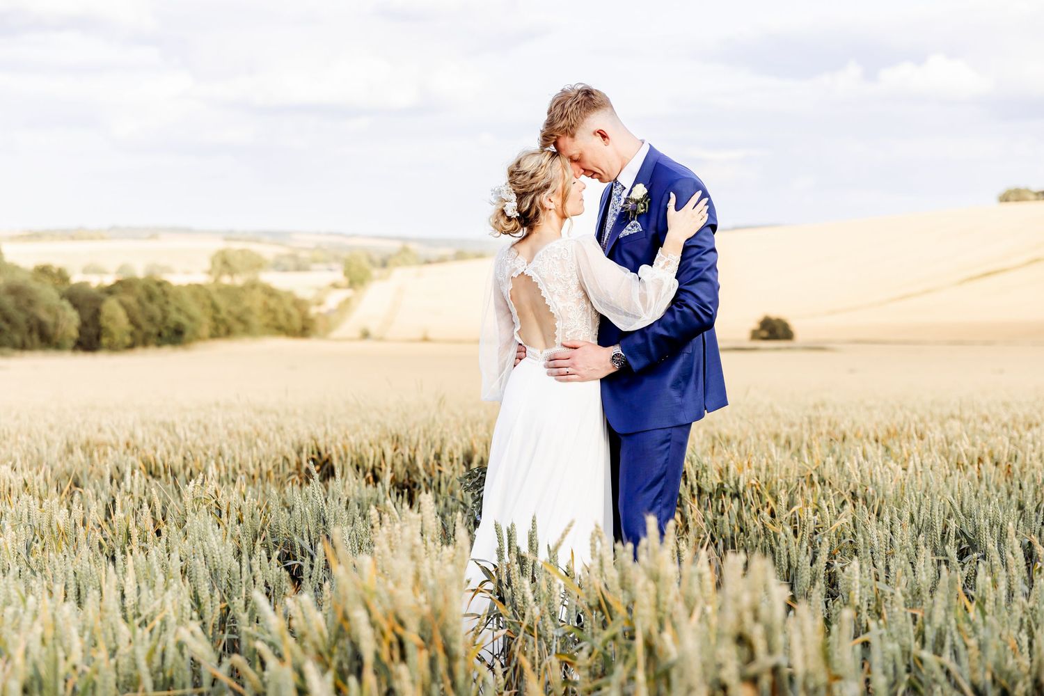 Bride and groom sharing a romantic kiss in a golden wheat field on their wedding day.