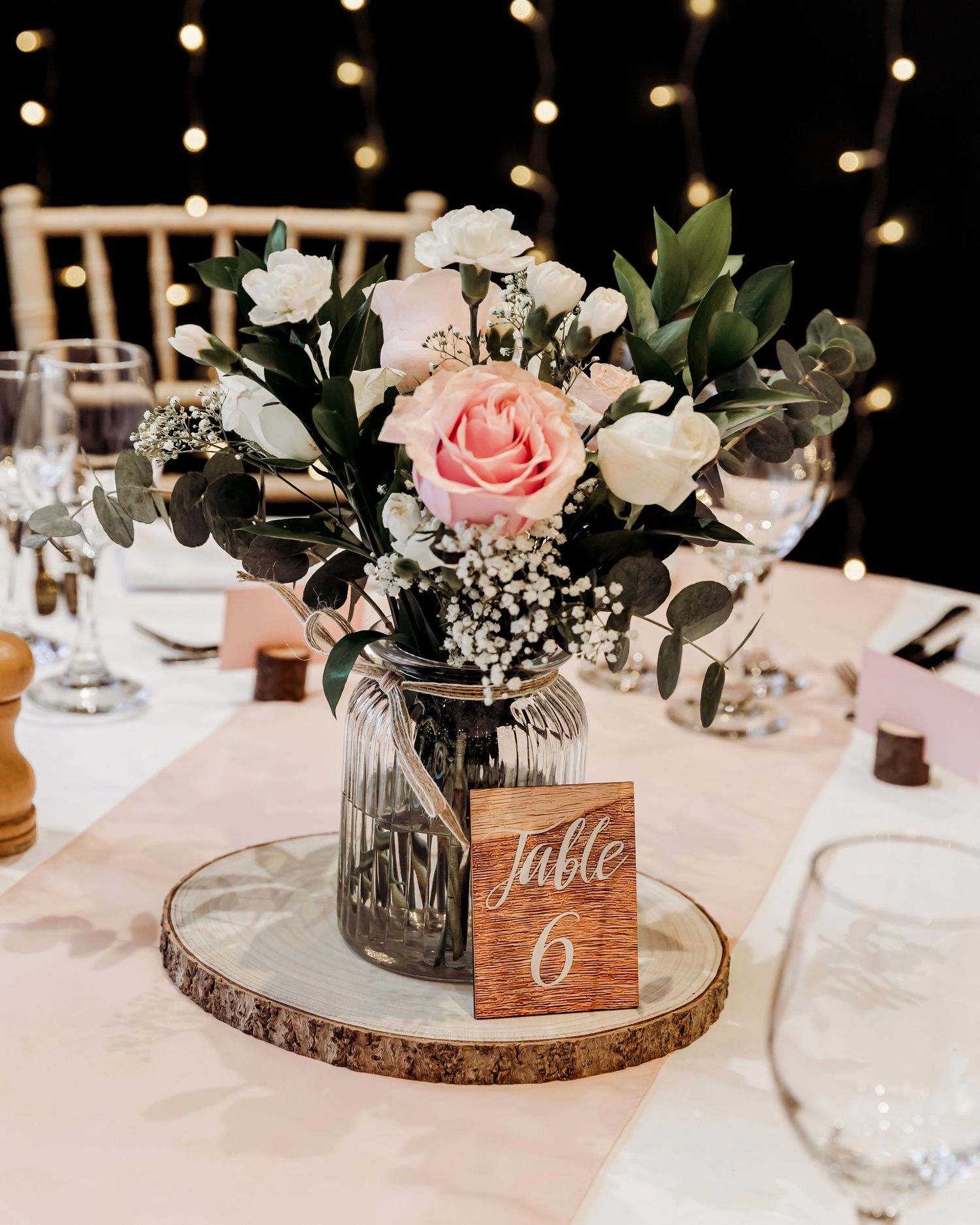 Rustic wedding table centerpiece with pink roses and white flowers in a mason jar on a wood slice.