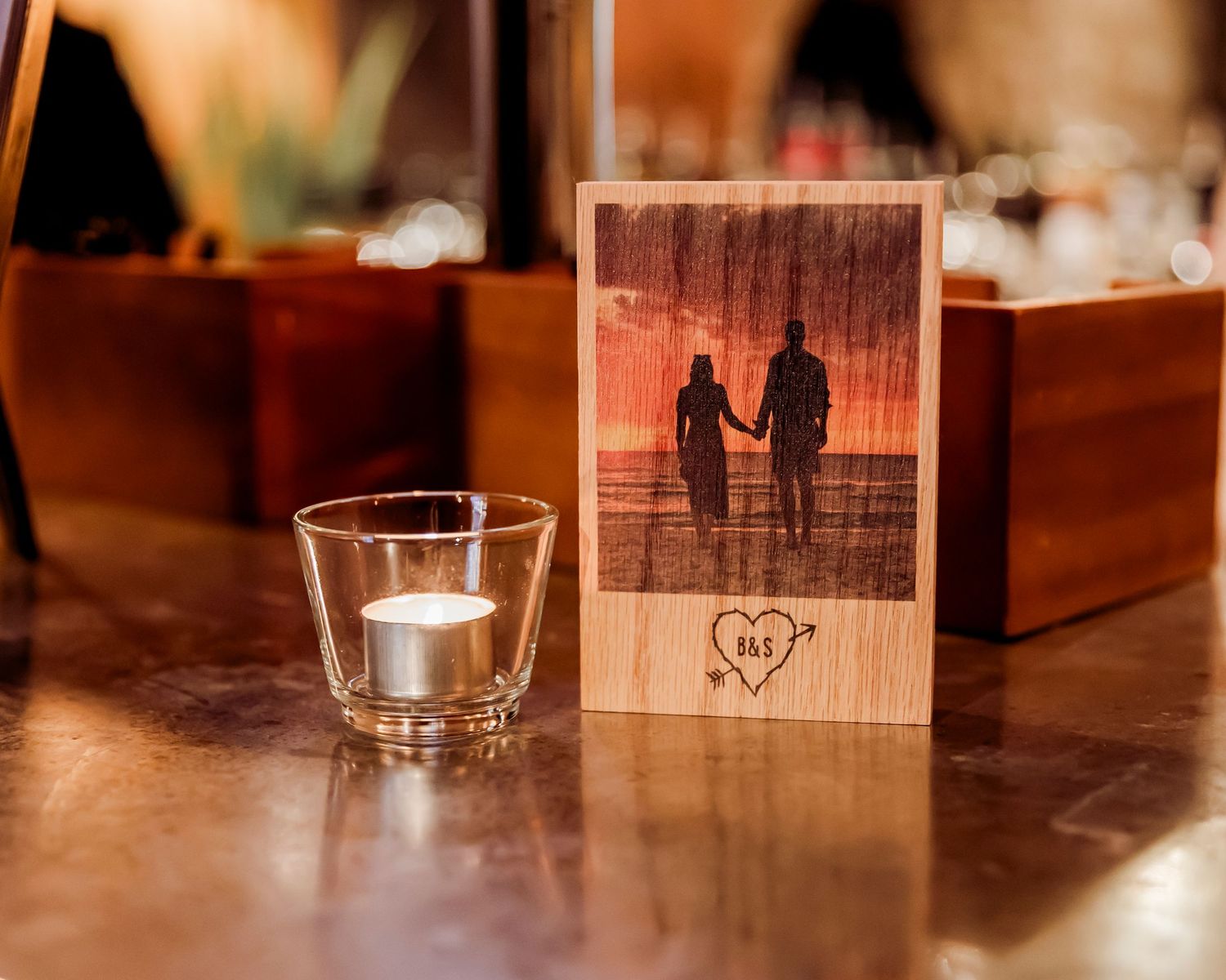 Engraved wooden photo block of couple at sunset beside a tealight candle.