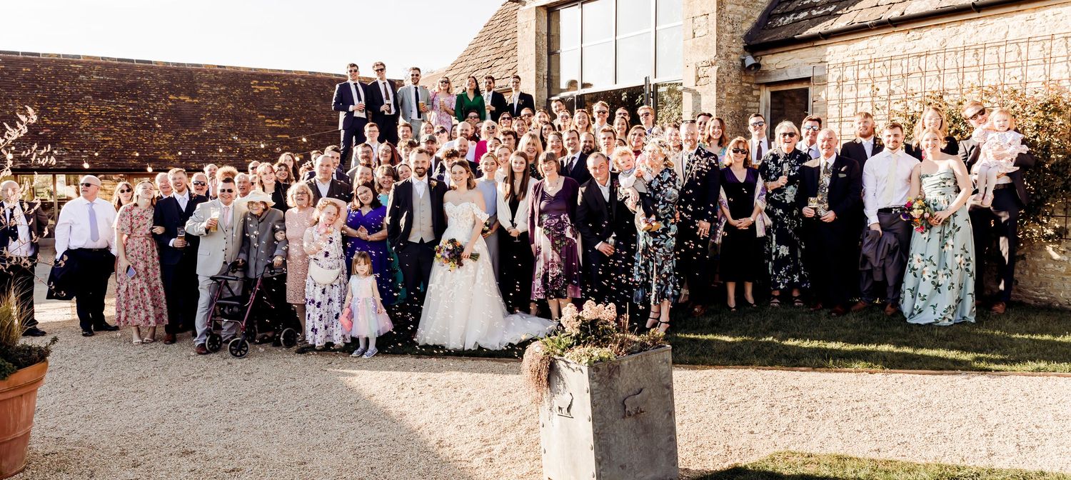 Large wedding group photo of all guests and couple gathered outside rustic stone countryside venue.