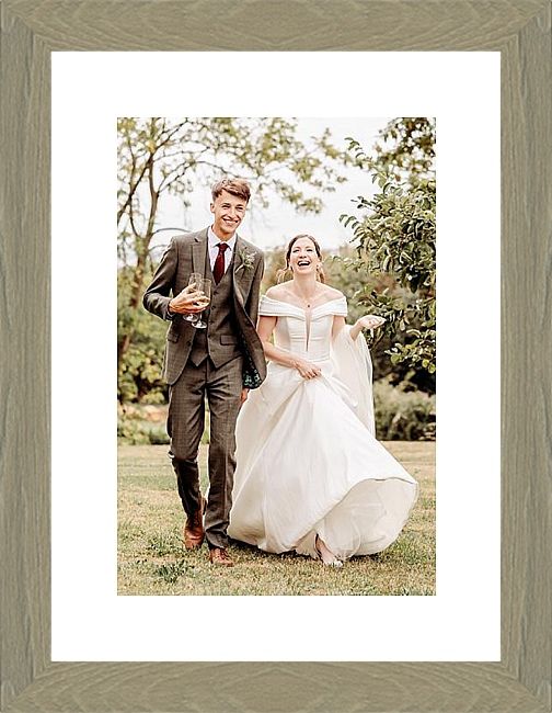 Laughing bride twirling white dress beside suited groom in grey wood frame with mount.
