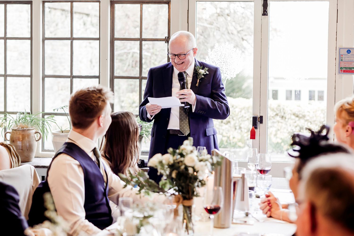Man in navy suit giving a speech at an elegant wedding reception dinner.