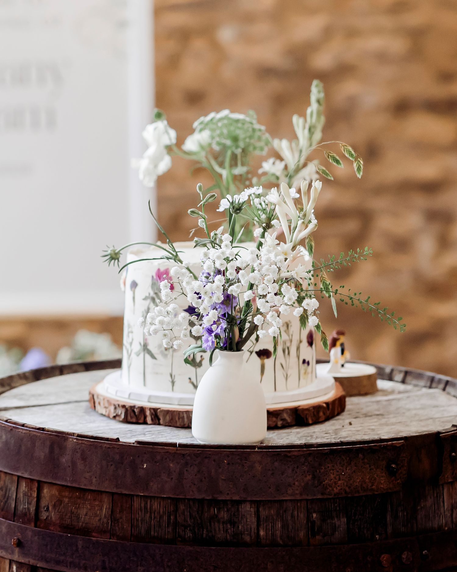 Rustic wedding cake with wildflowers on a wooden barrel slice centerpiece display.